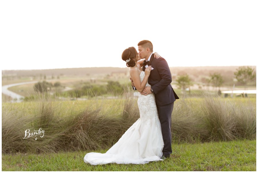 bride and groom kissing in open field at sunset