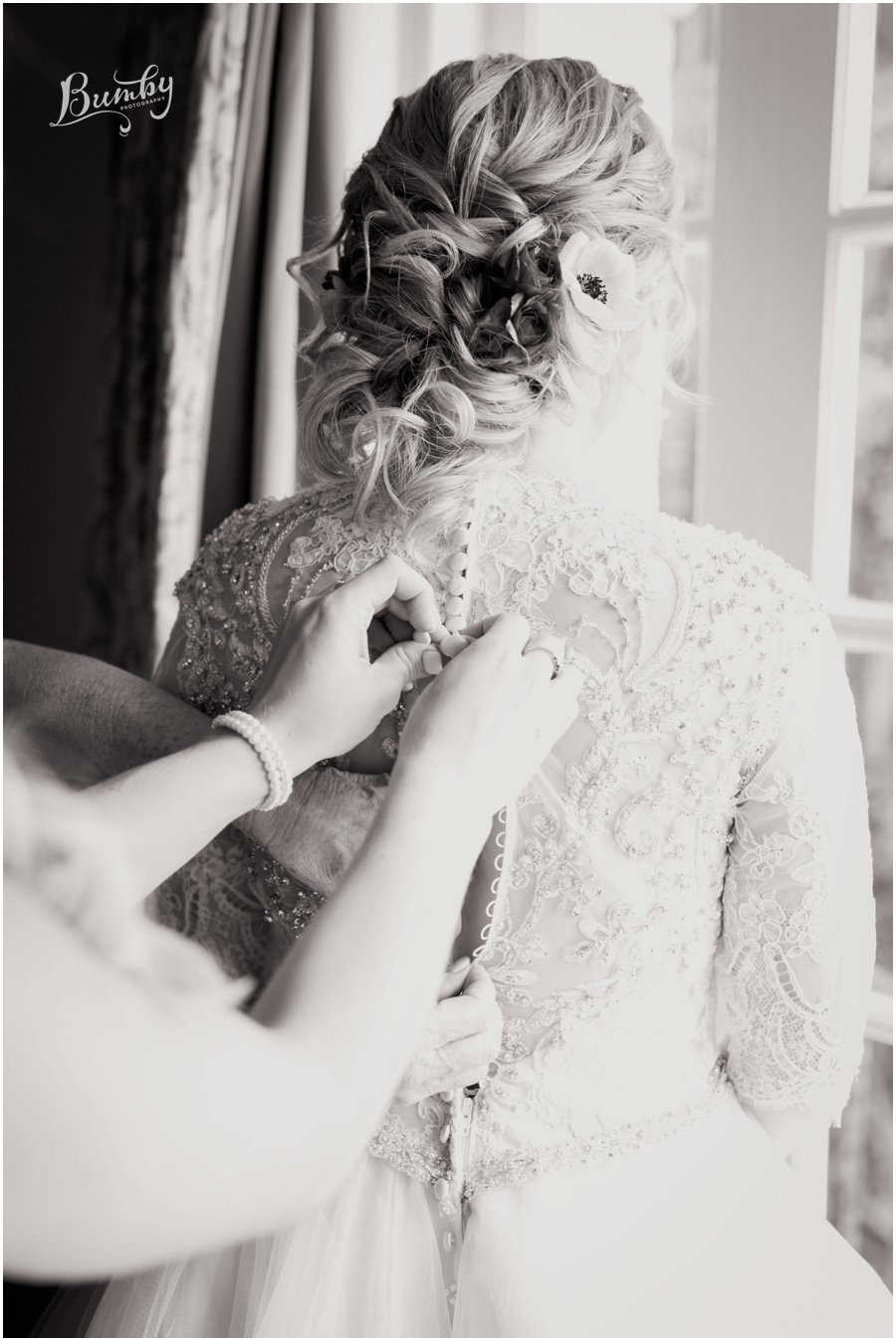 Black and white photo of the bride having her dress buttoned up.
