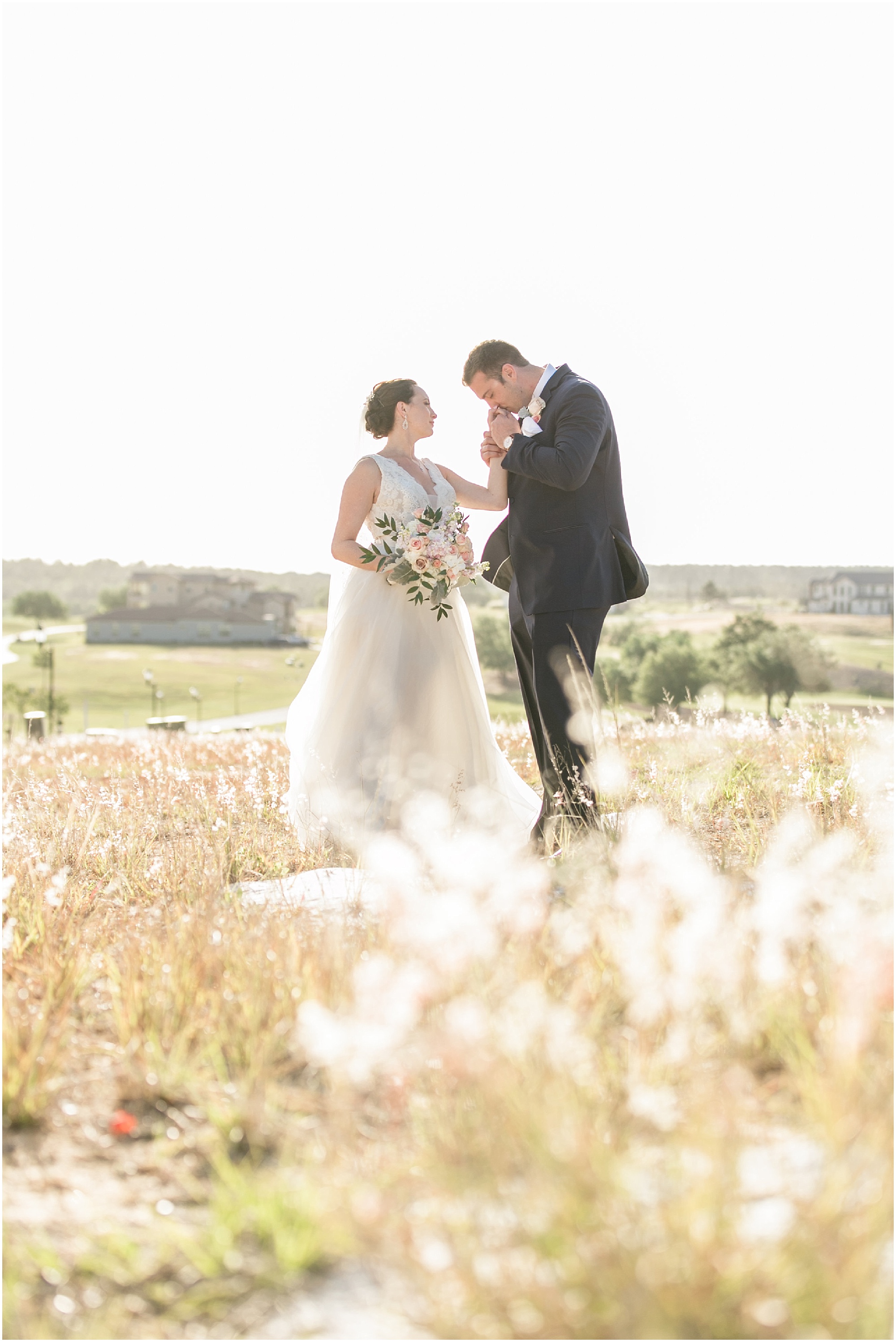 Groom kissing brides hand in field at Bella Collina