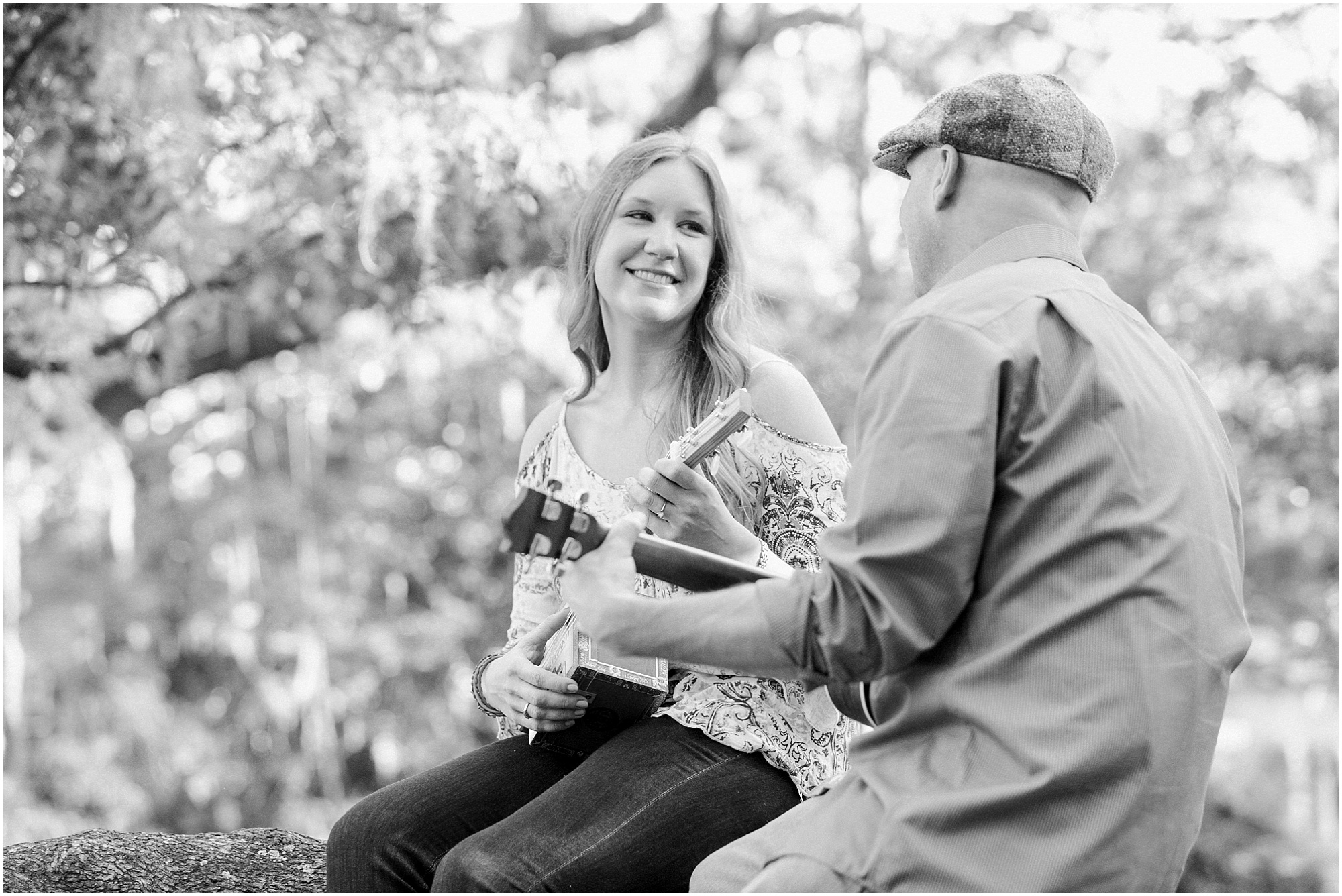 Woman looking at guy while he is playing the guitar in a tree outdoors.