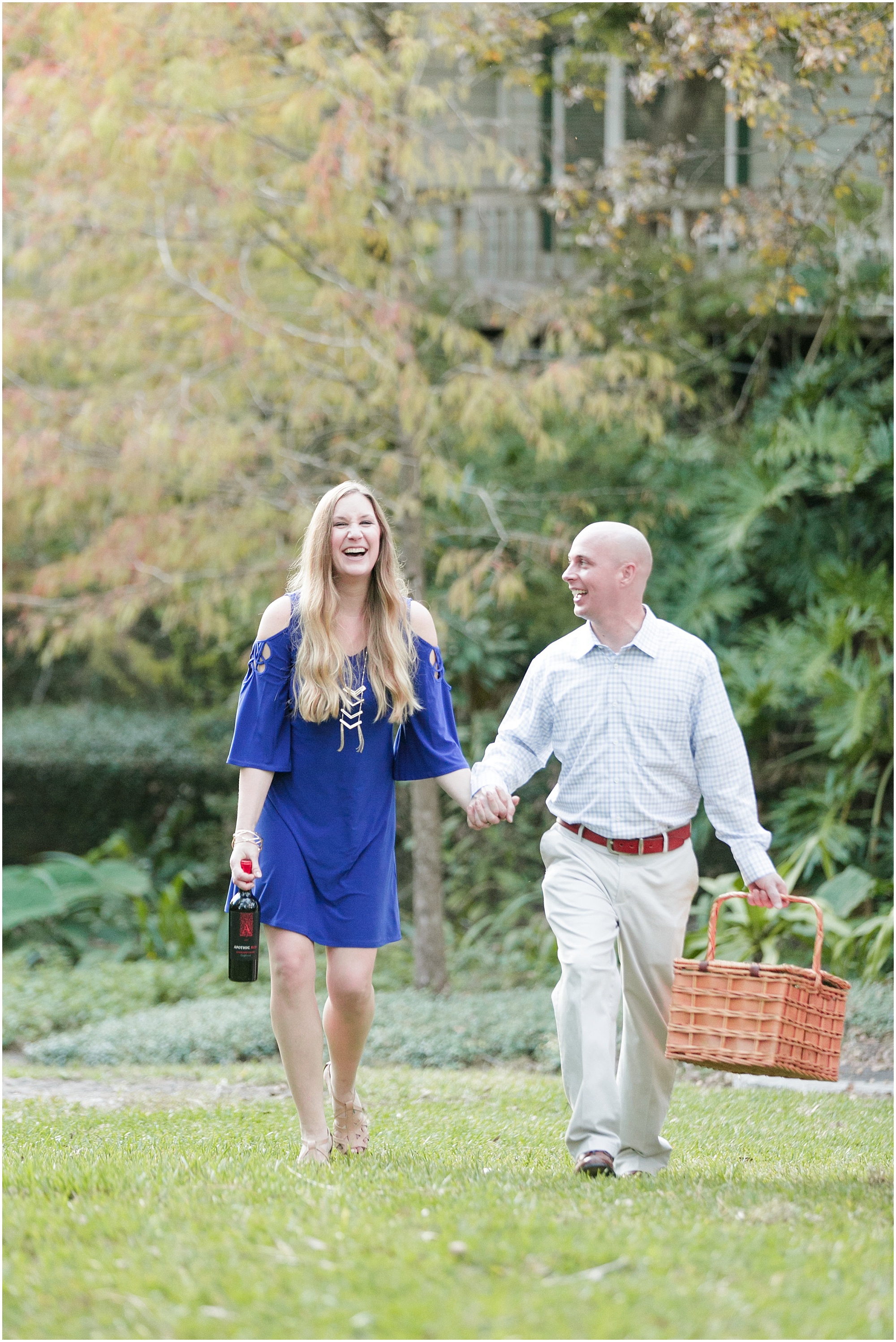 Musical outdoor laughing couple walking while holding a picnic basket and wine.