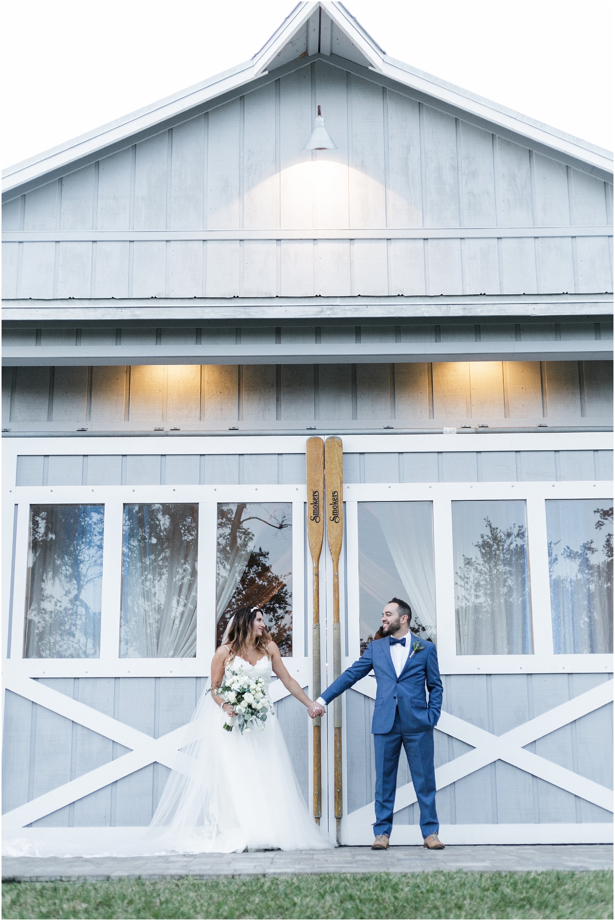Bride and groom holding hands at country farm boathouse doors
