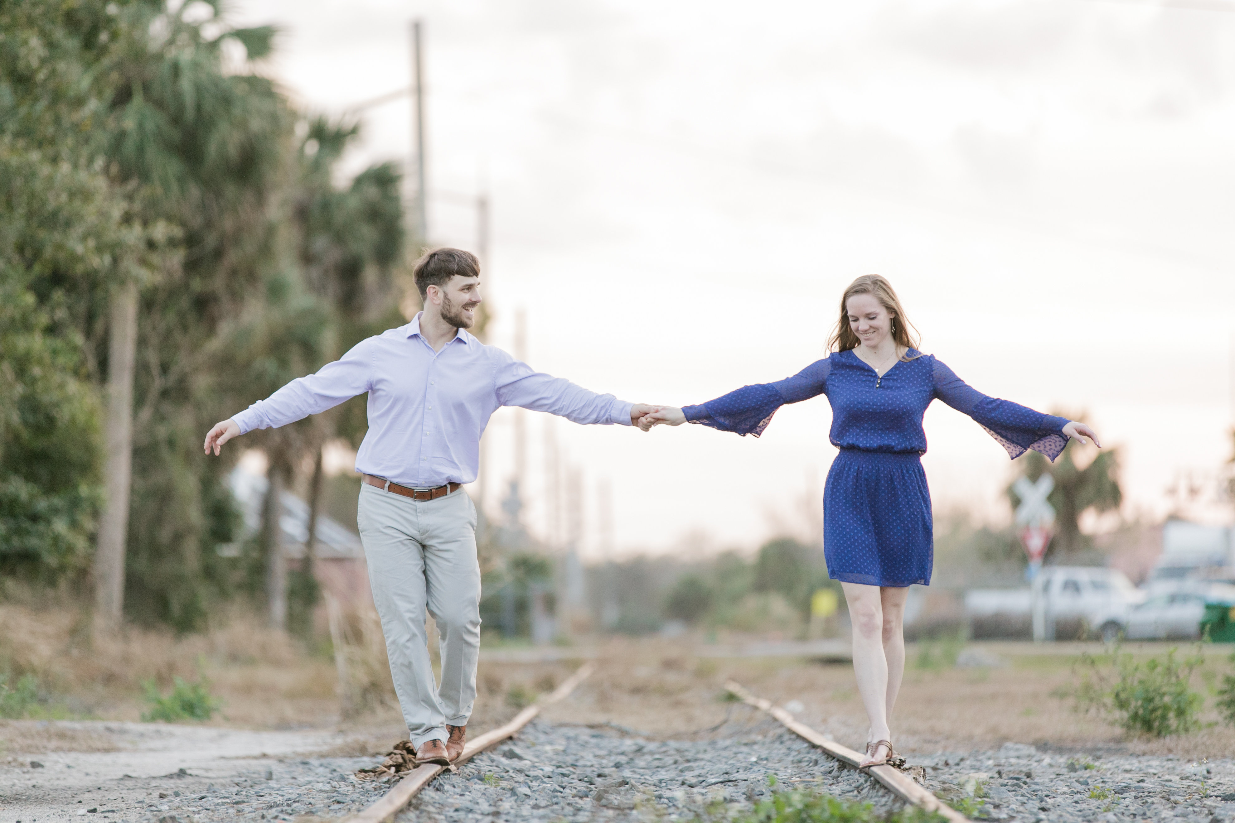Engagement session couple holding hands while walking on empty railroad tracks.