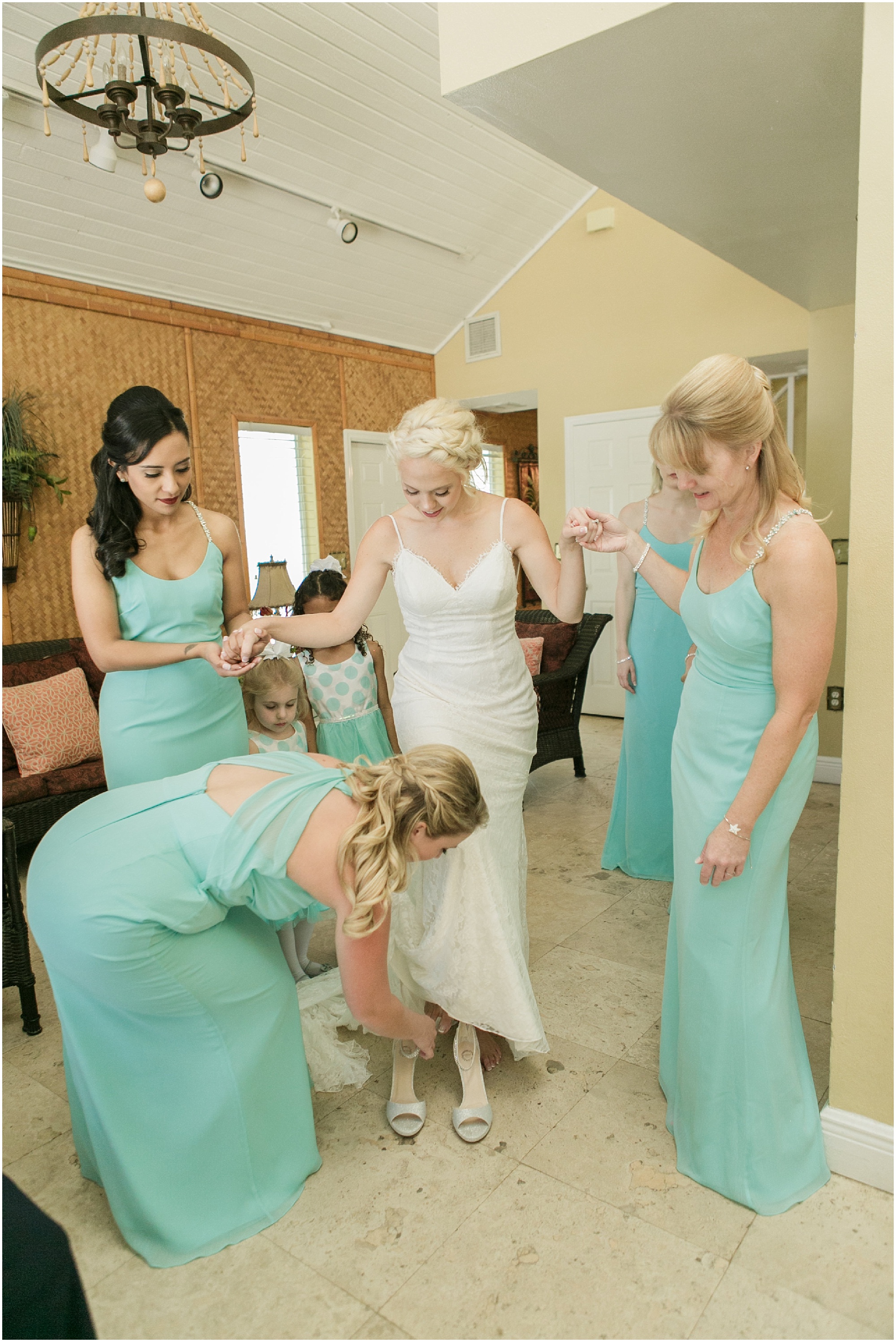 Bridesmaids holding bride's hands as she puts on her shoes