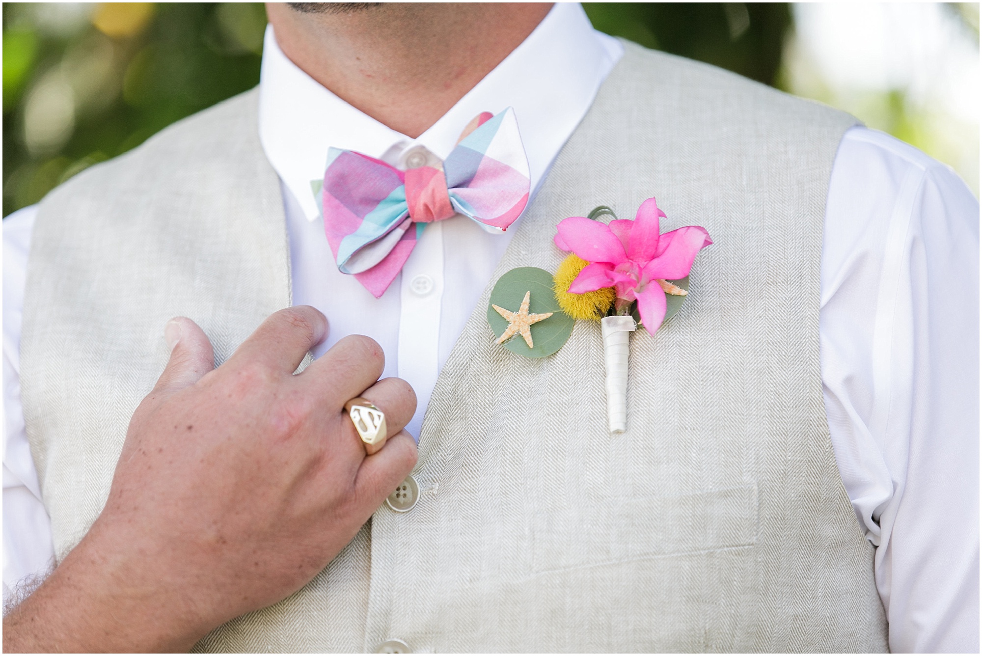 Grooms accessories including pink plaid bowtie, pink and yellow boutonnière, and gold ring. 