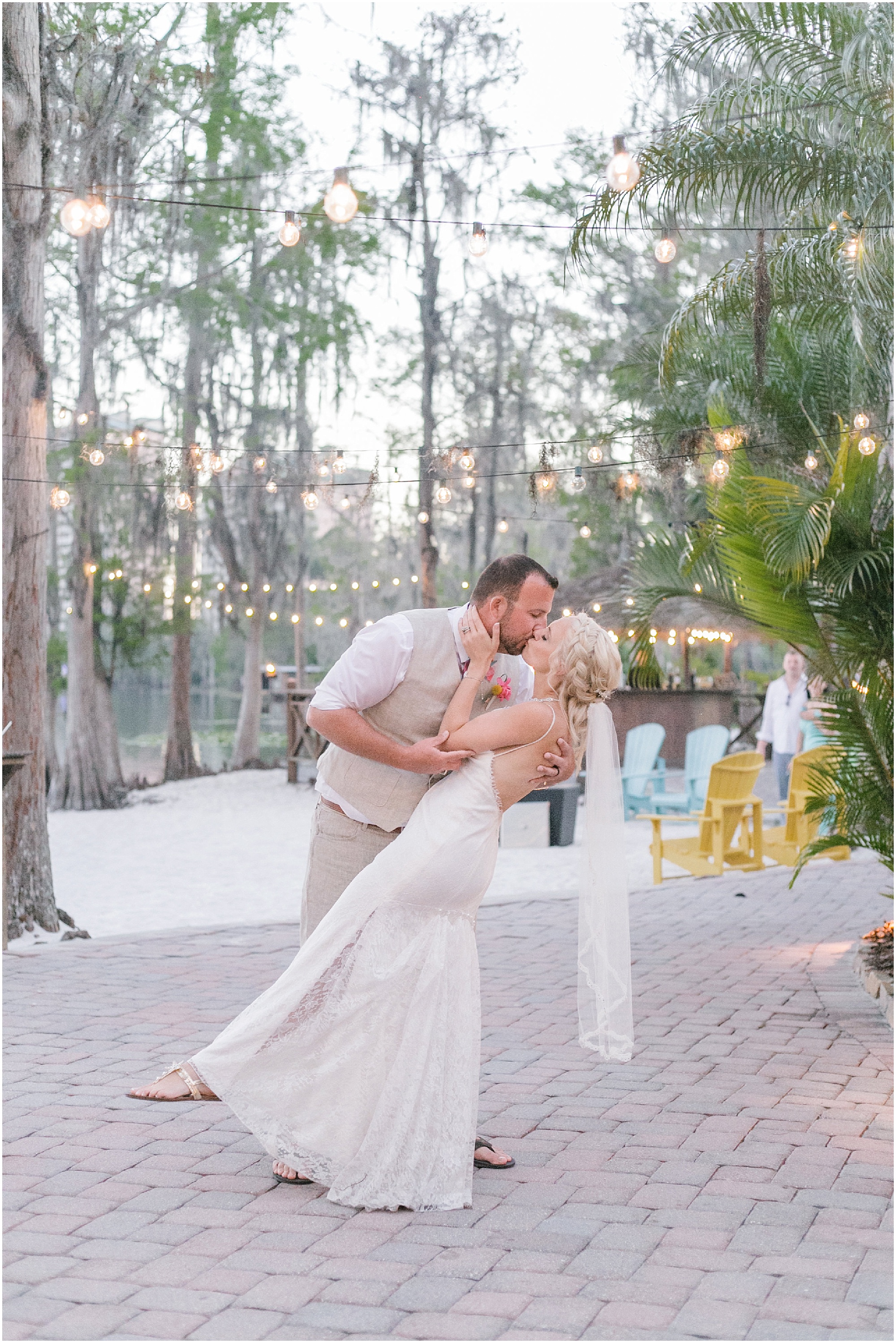 Husband dips his bride and gives her a kiss under patio lights.