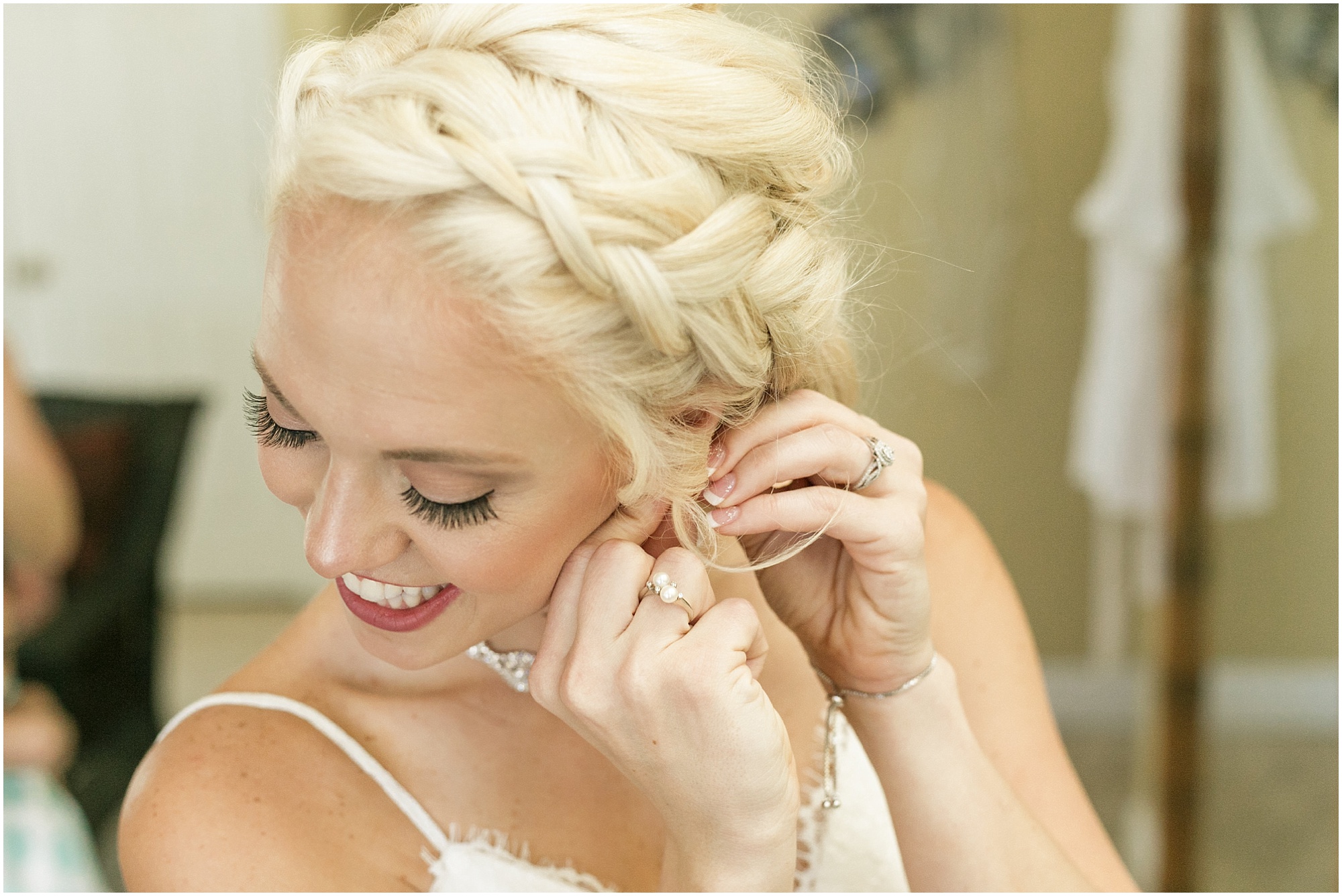 Bride putting on her earring on her left ear and smiling. 