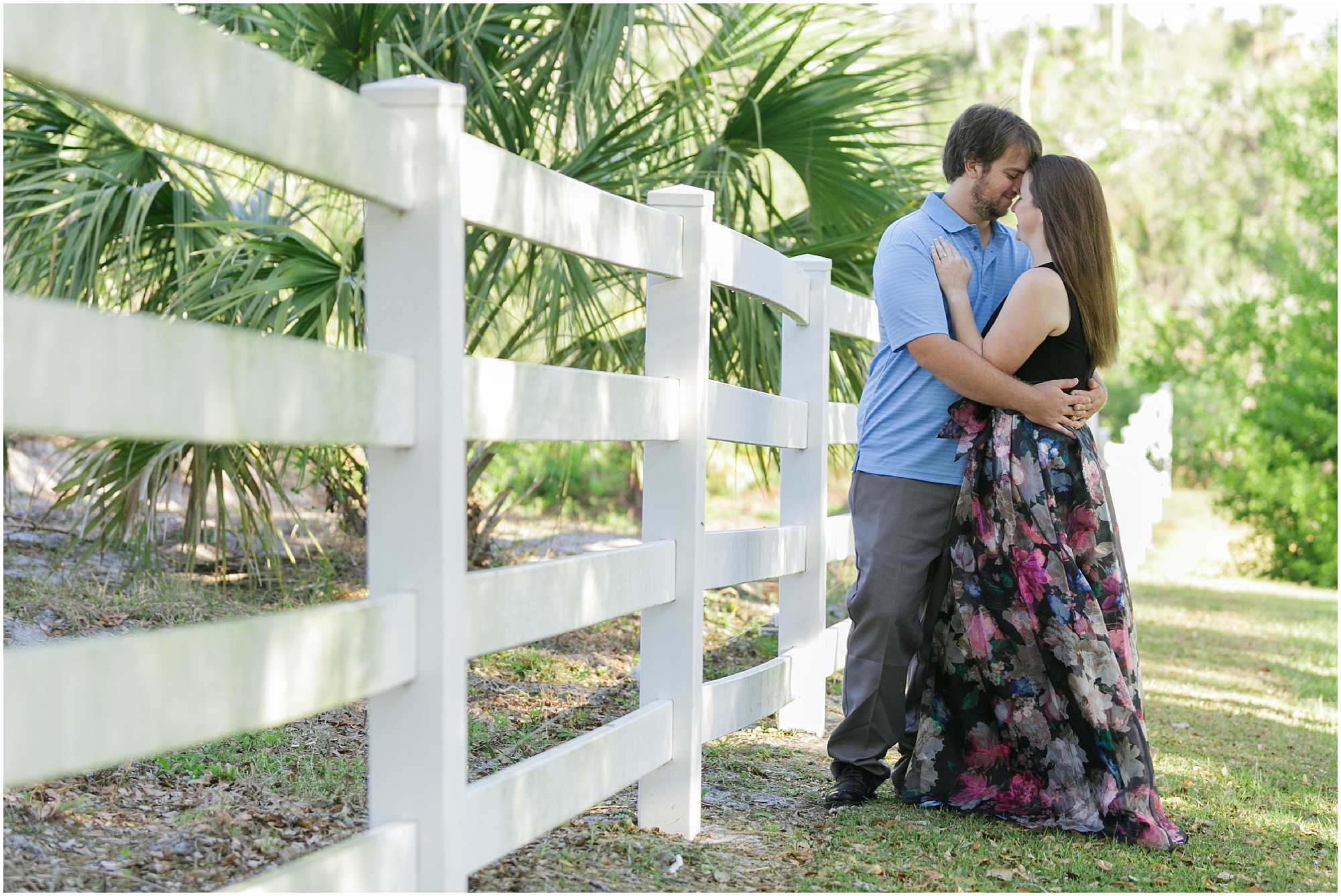 Couple hugging next to a white barn fence. 