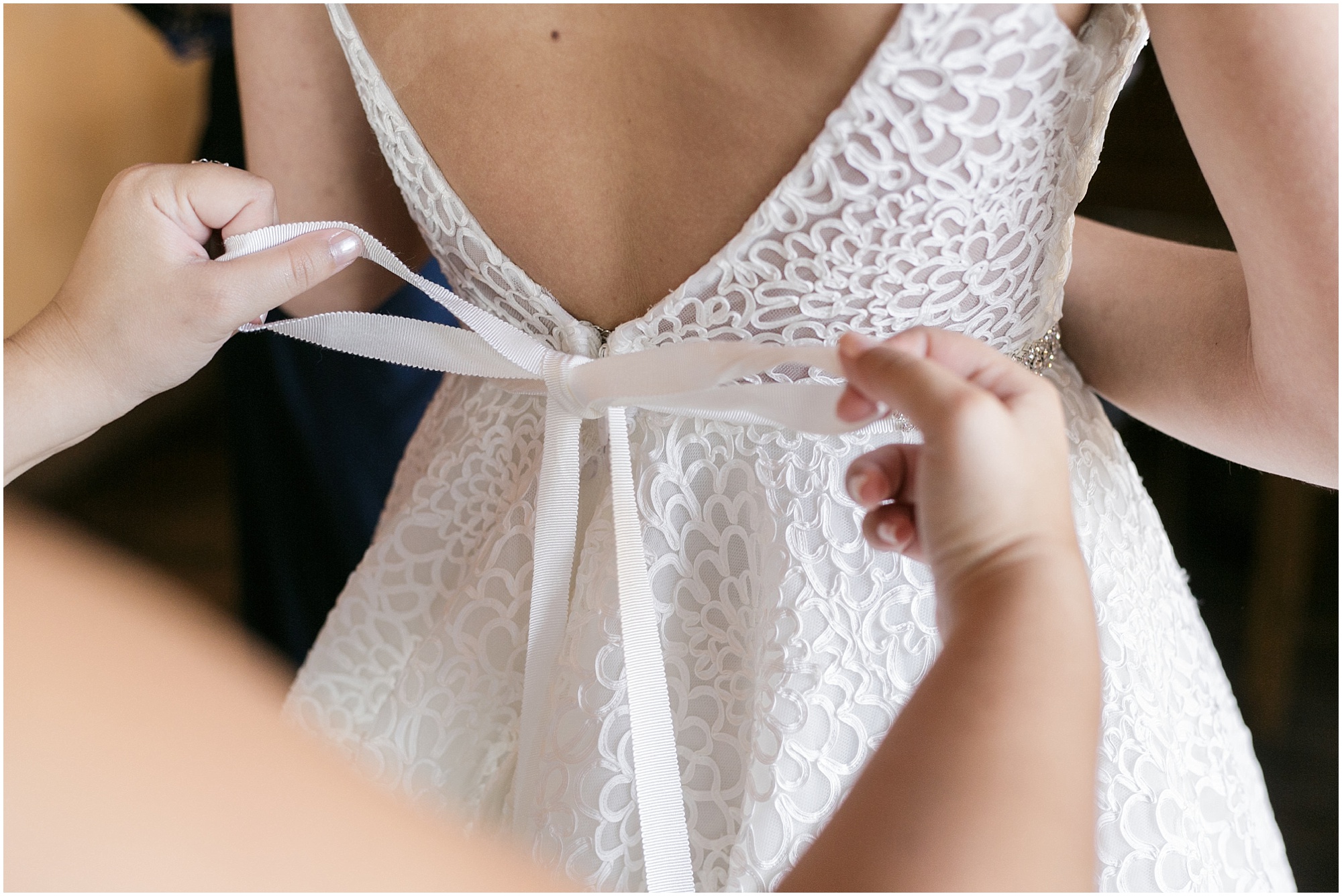 Bridesmaid tying the ribbon on the back of the wedding dress.