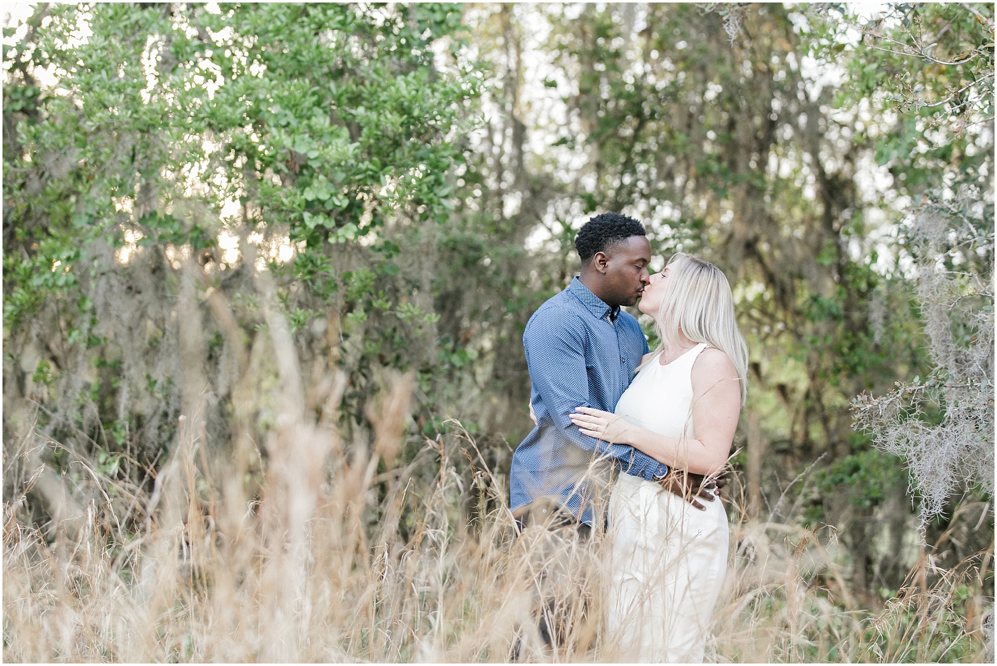 Lake Nona Engagement couple standing in tall grass with trees behind them.