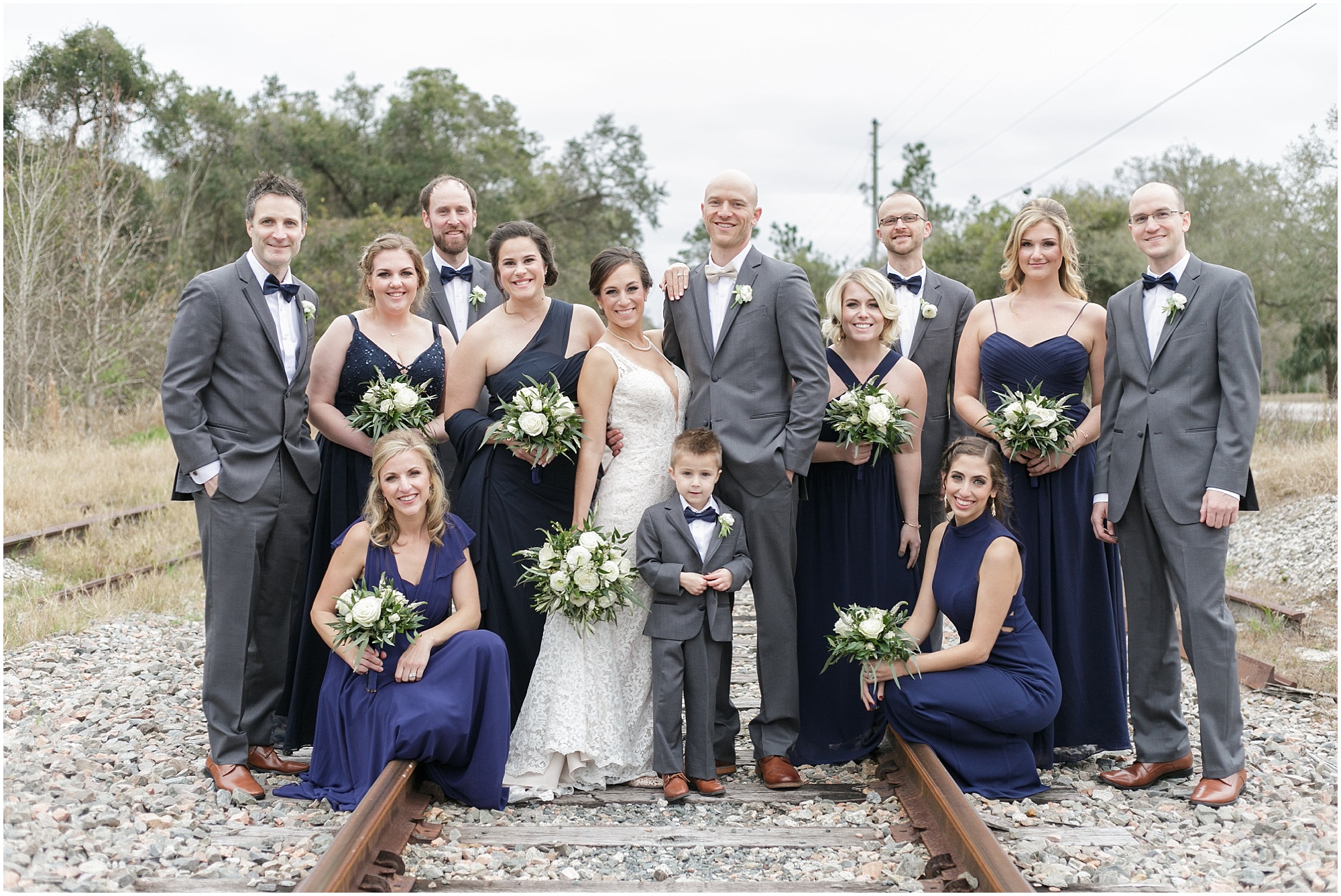 The entire wedding party posing with the bride and the groom on abandoned railroad tracks.