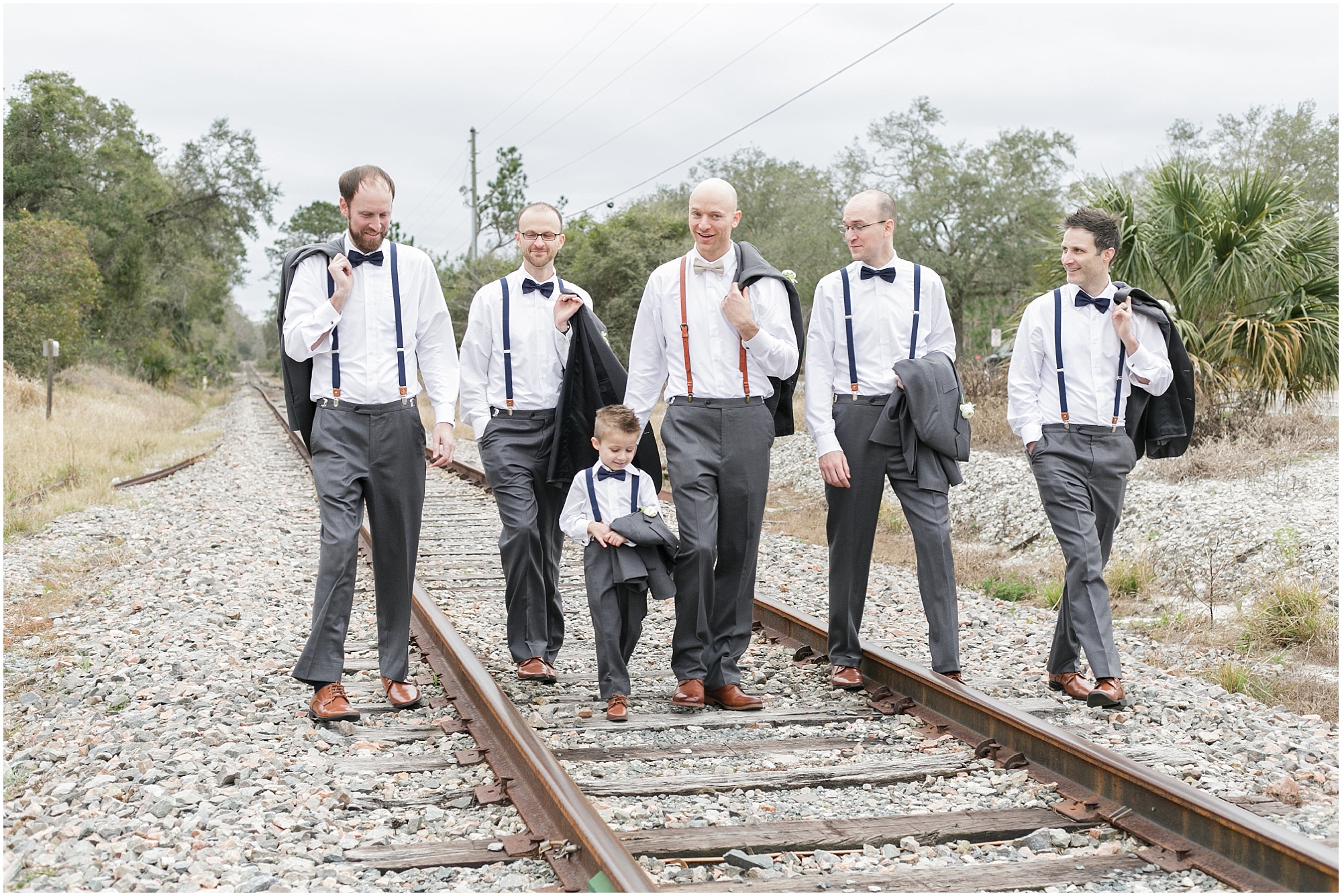 Groom and his groomsmen walking along the railroad tracks.