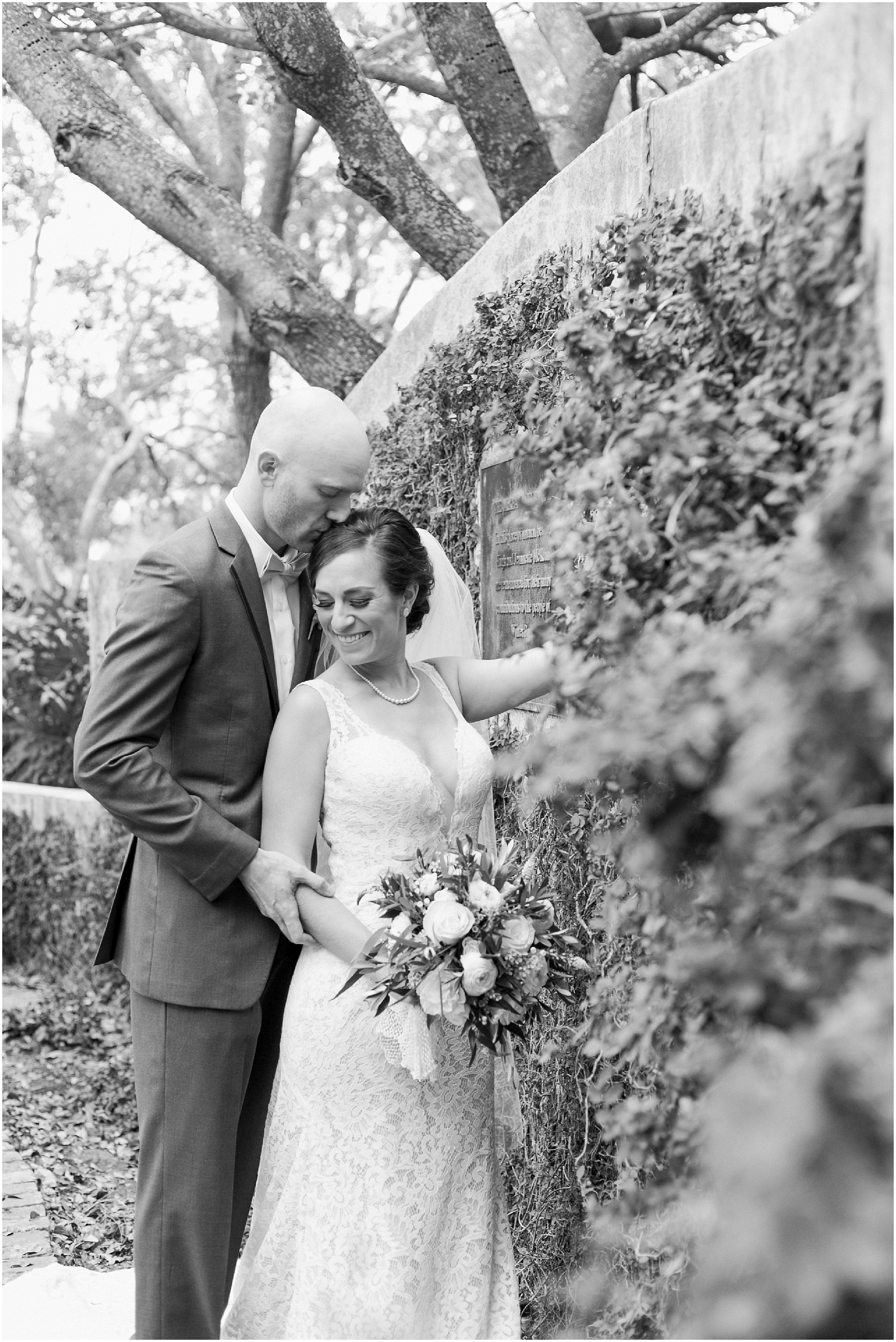 Black and white photo of the bride and groom taking photos next to a wall covered in vines.