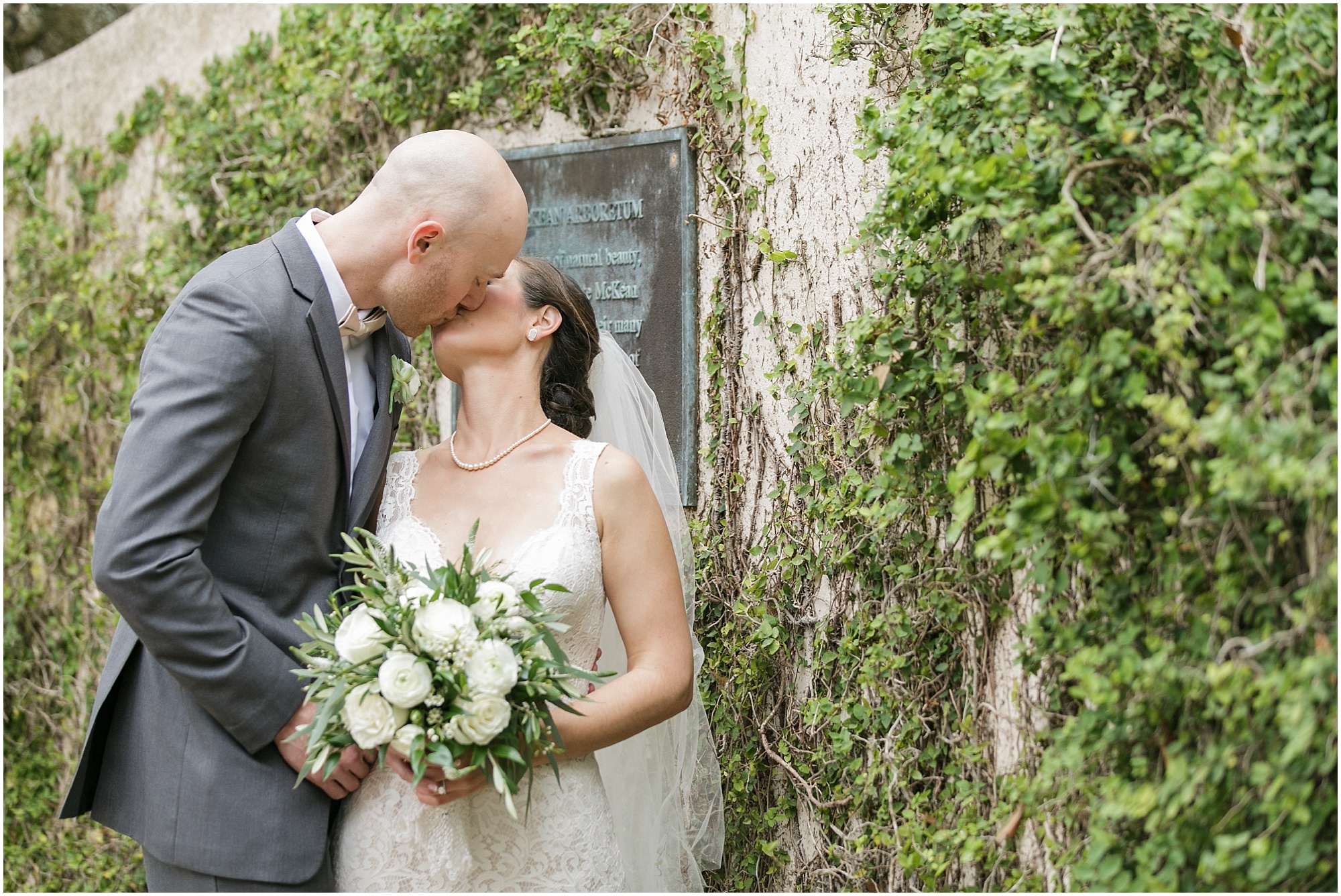 Bride and Groom kissing while standing next to a wall covered in vines.
