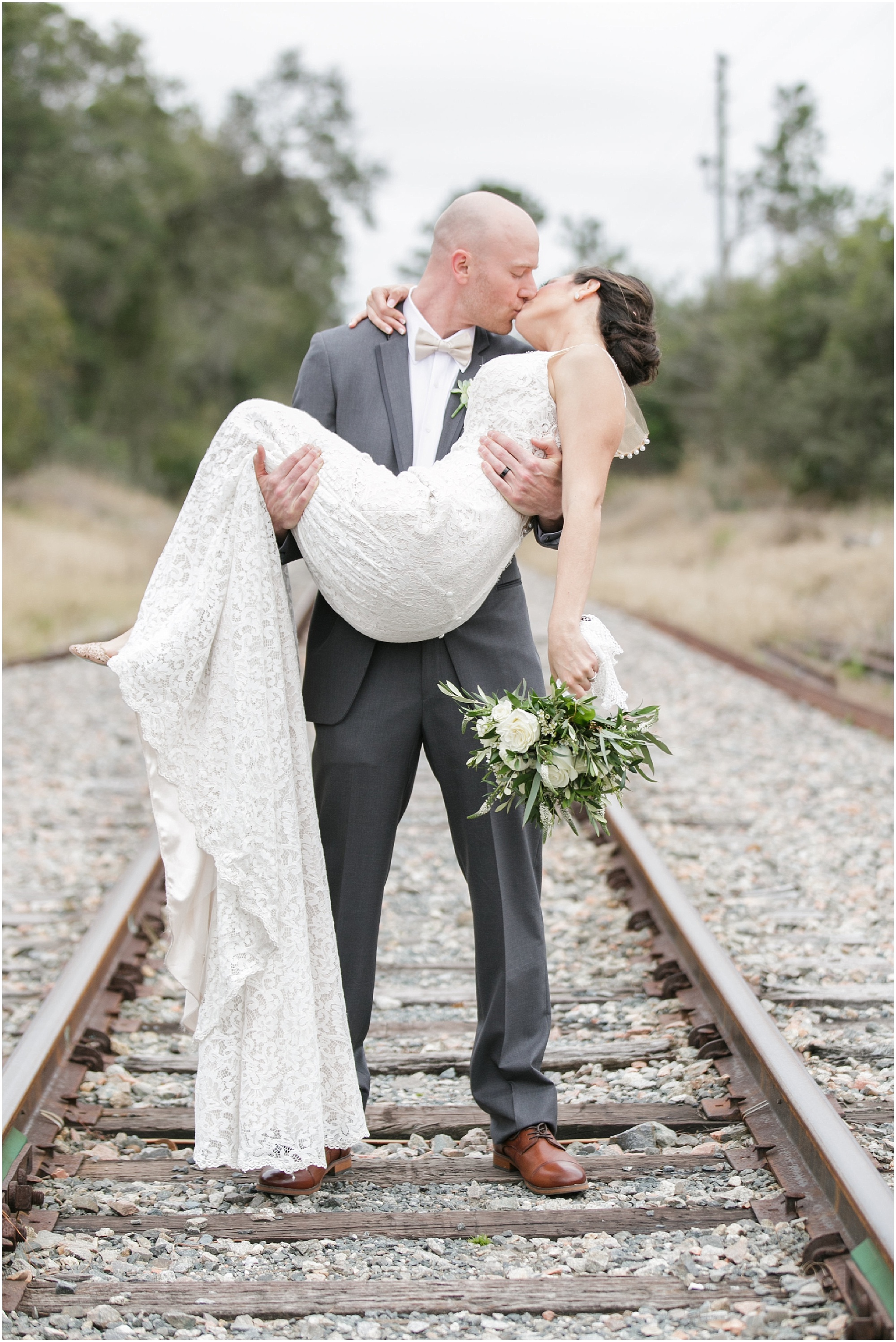 Groom kisses his bride while lifting her in his arms.
