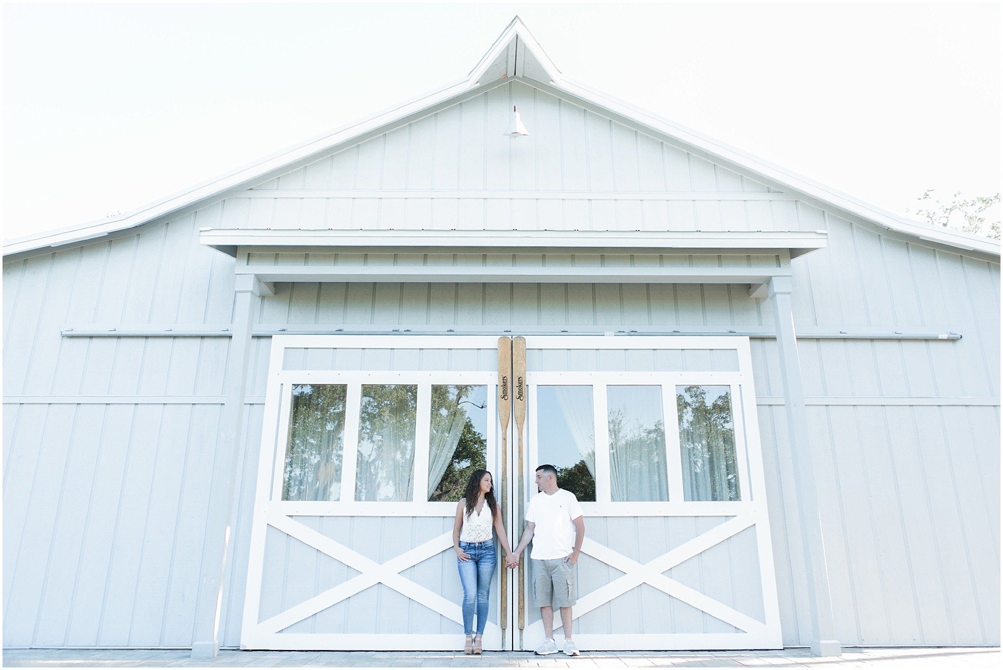 Couple holding hands and looking at each other while standing in front of boathouse doors at Up the Creek Farms. 