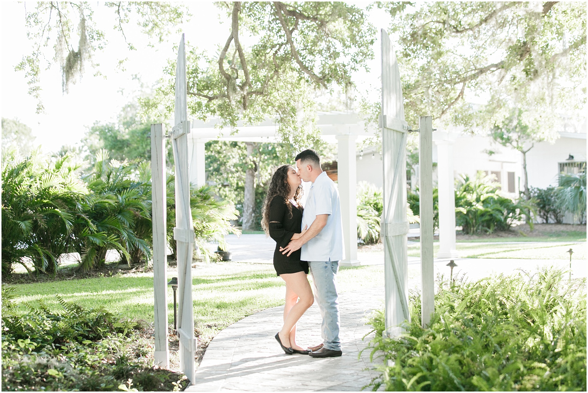 Engaged couple kissing while standing inside of a white fence. 