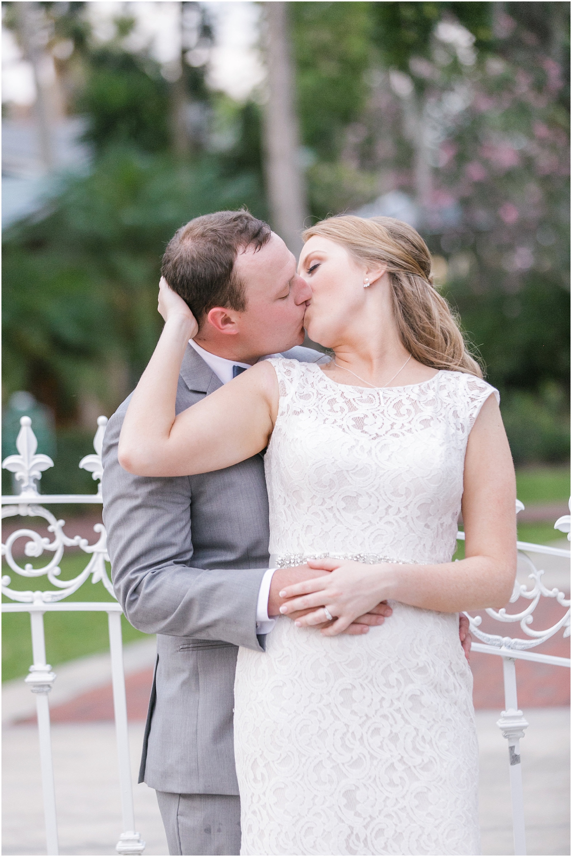 Bride and groom kissing each other with a white iron fence behind them.