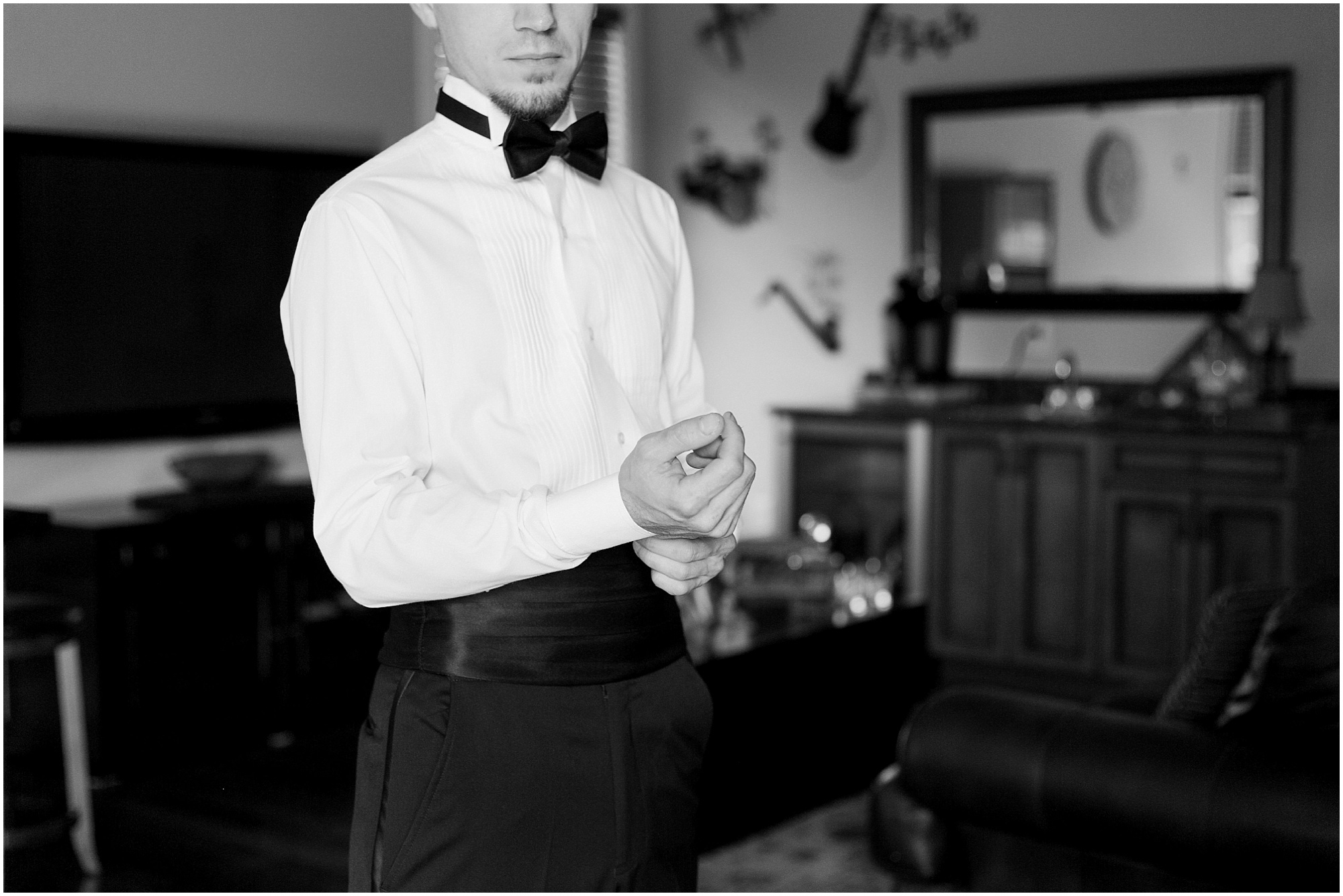 Black and white photo of the groom buttoning his shirt.