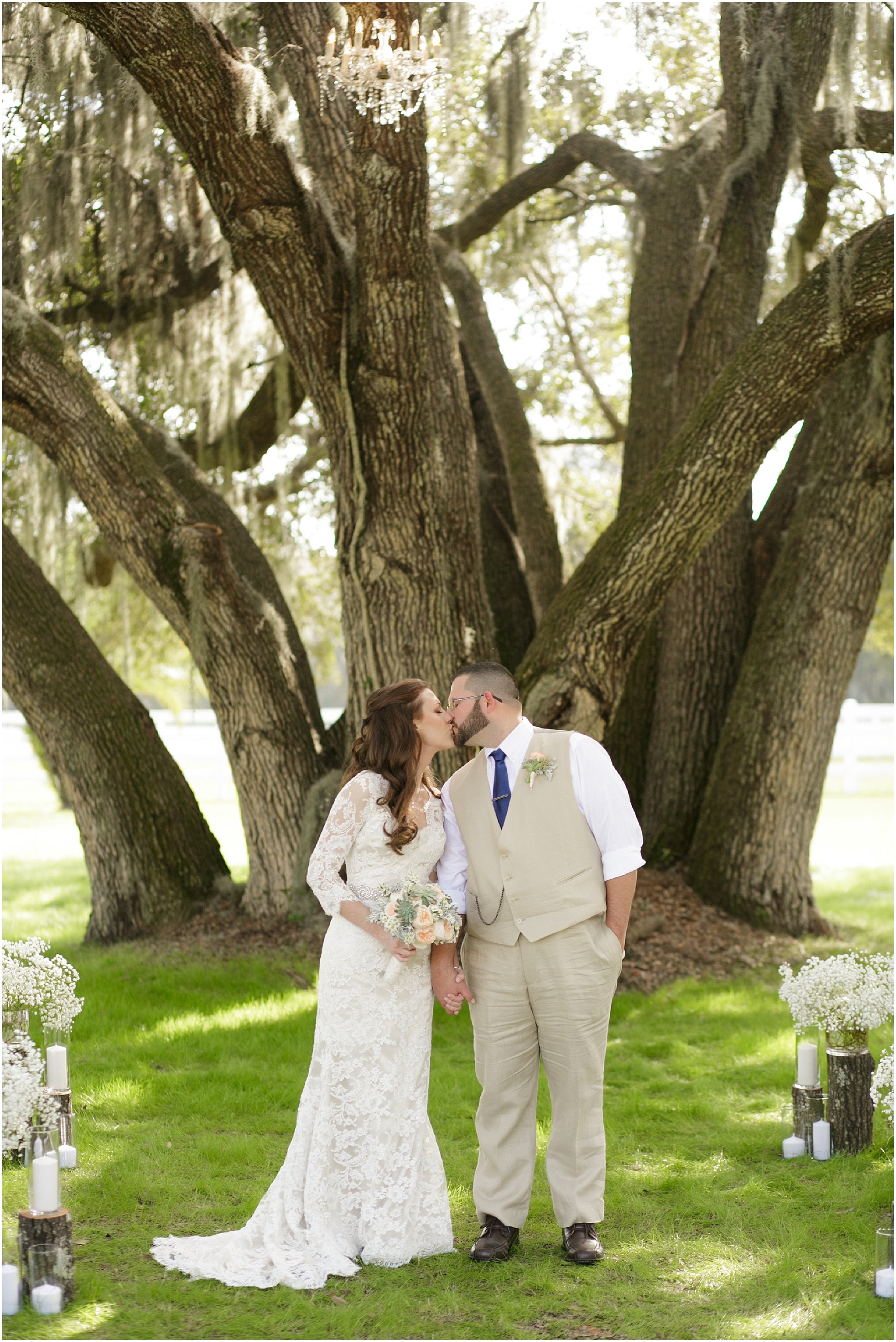 Bride and groom sharing a kiss under a large oak tree at their wedding ceremony.