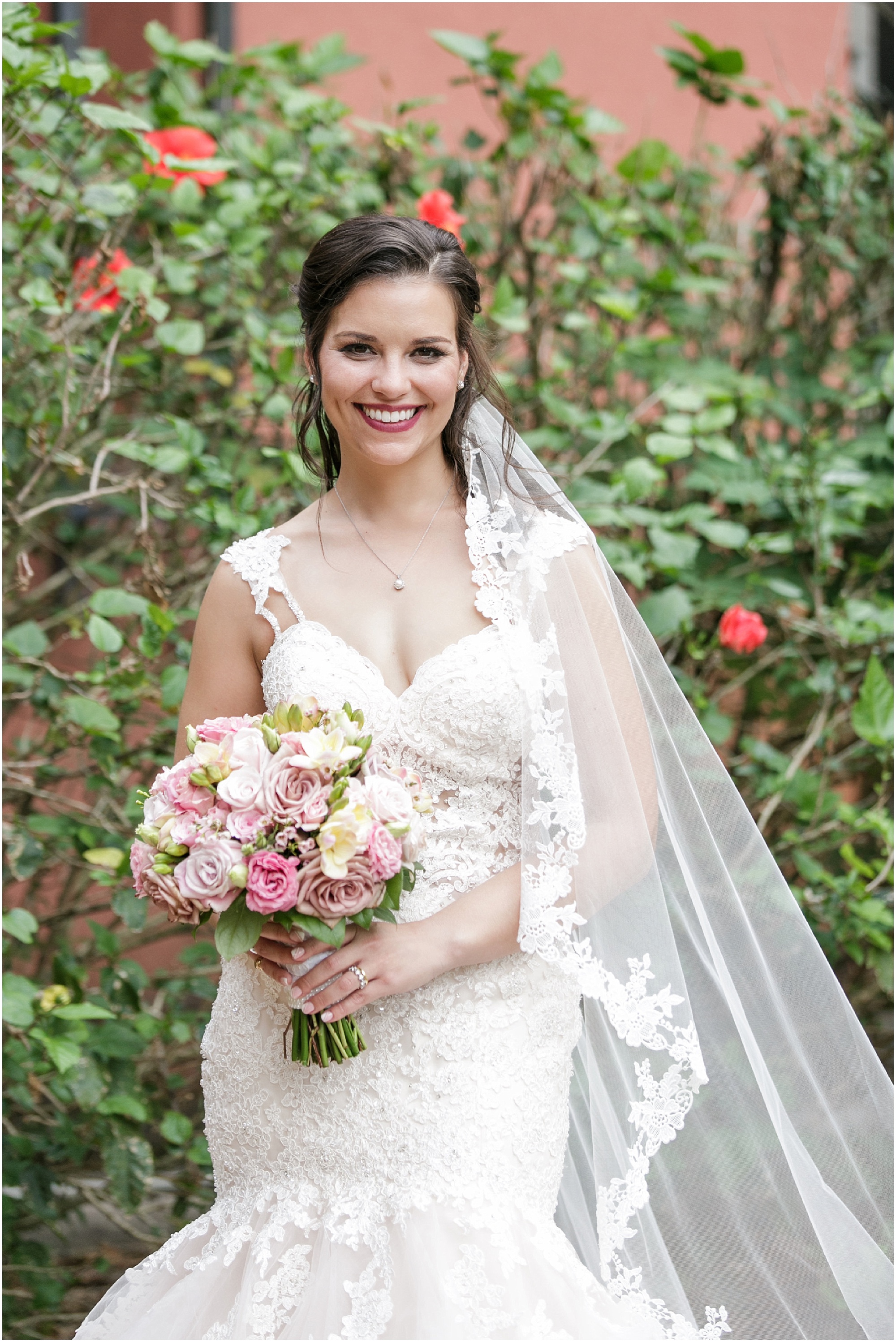 Bride smiling at the camera while she stands in front of green plants. 