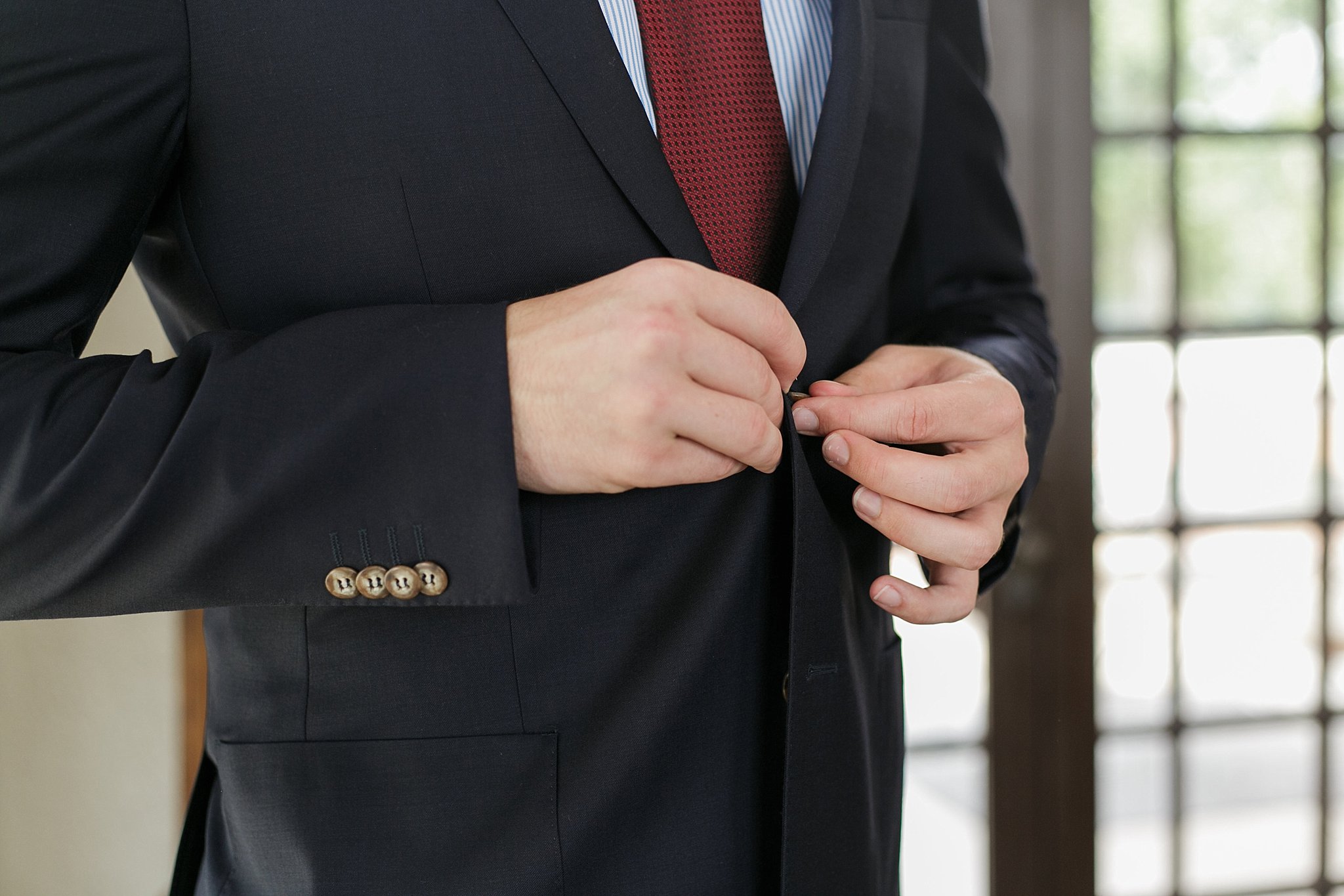 Groom buttoning up his jacket. 