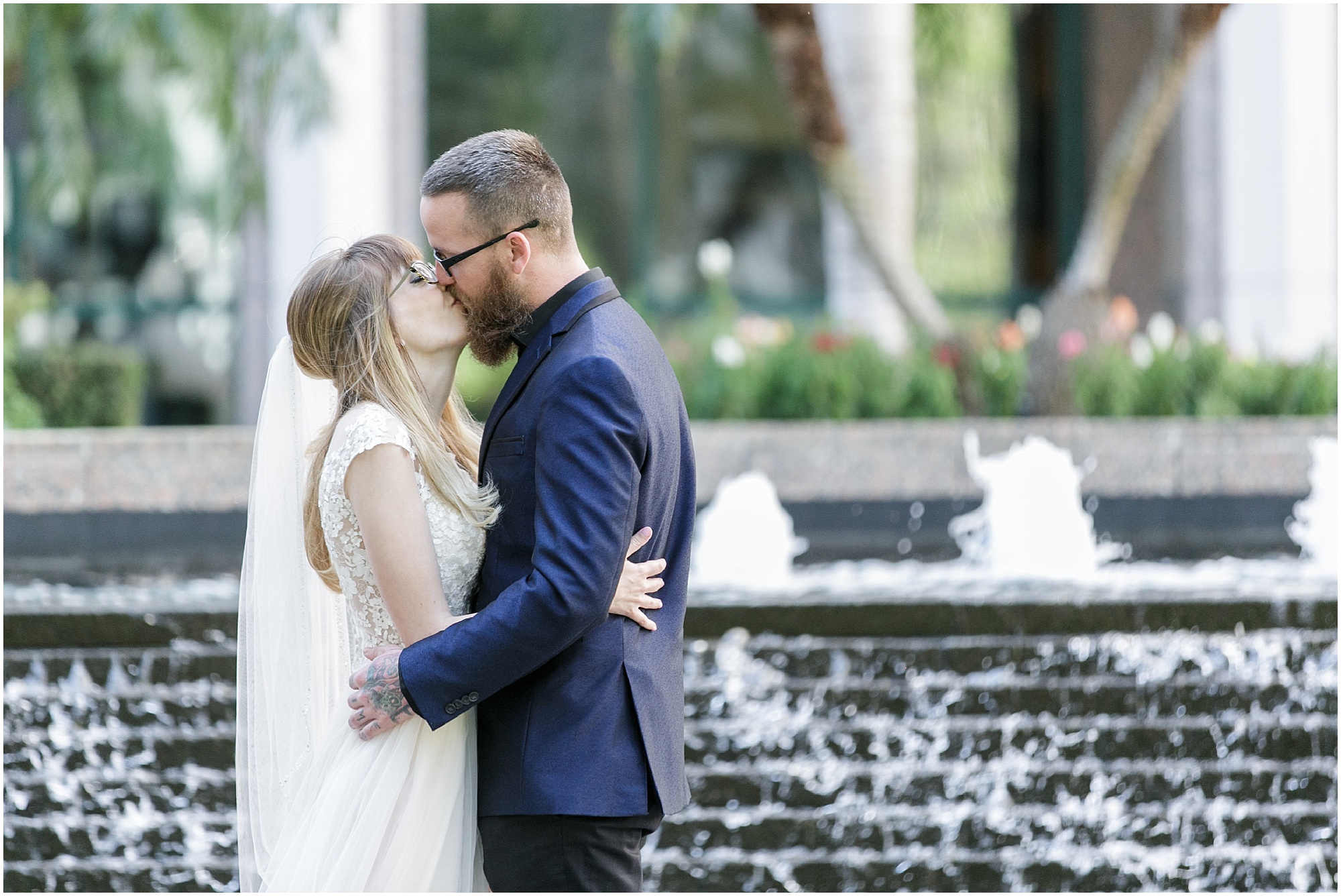 Bride and groom kissing while standing in front of a fountain.