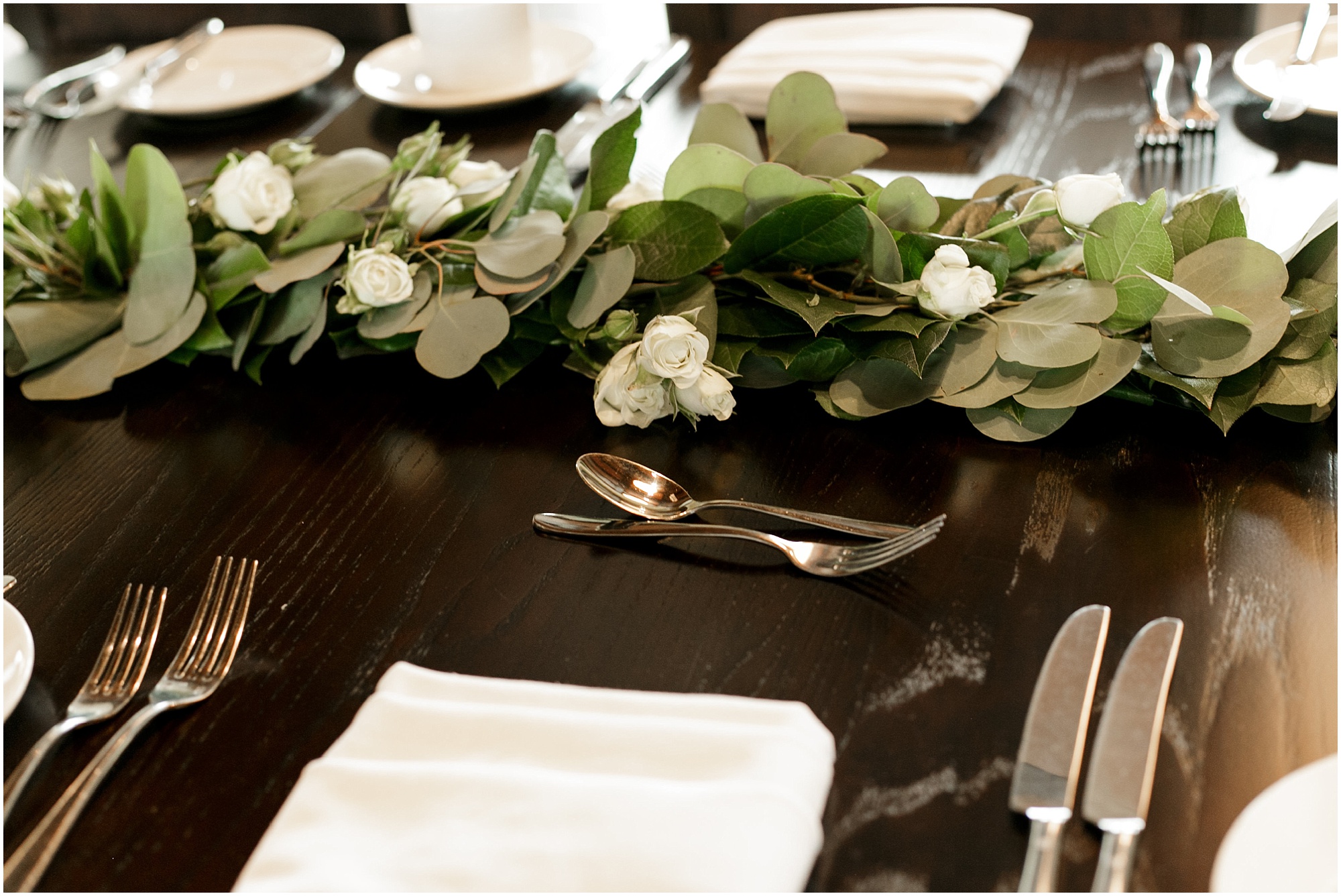 Place setting at reception including a centerpiece of greenery and white flowers. 