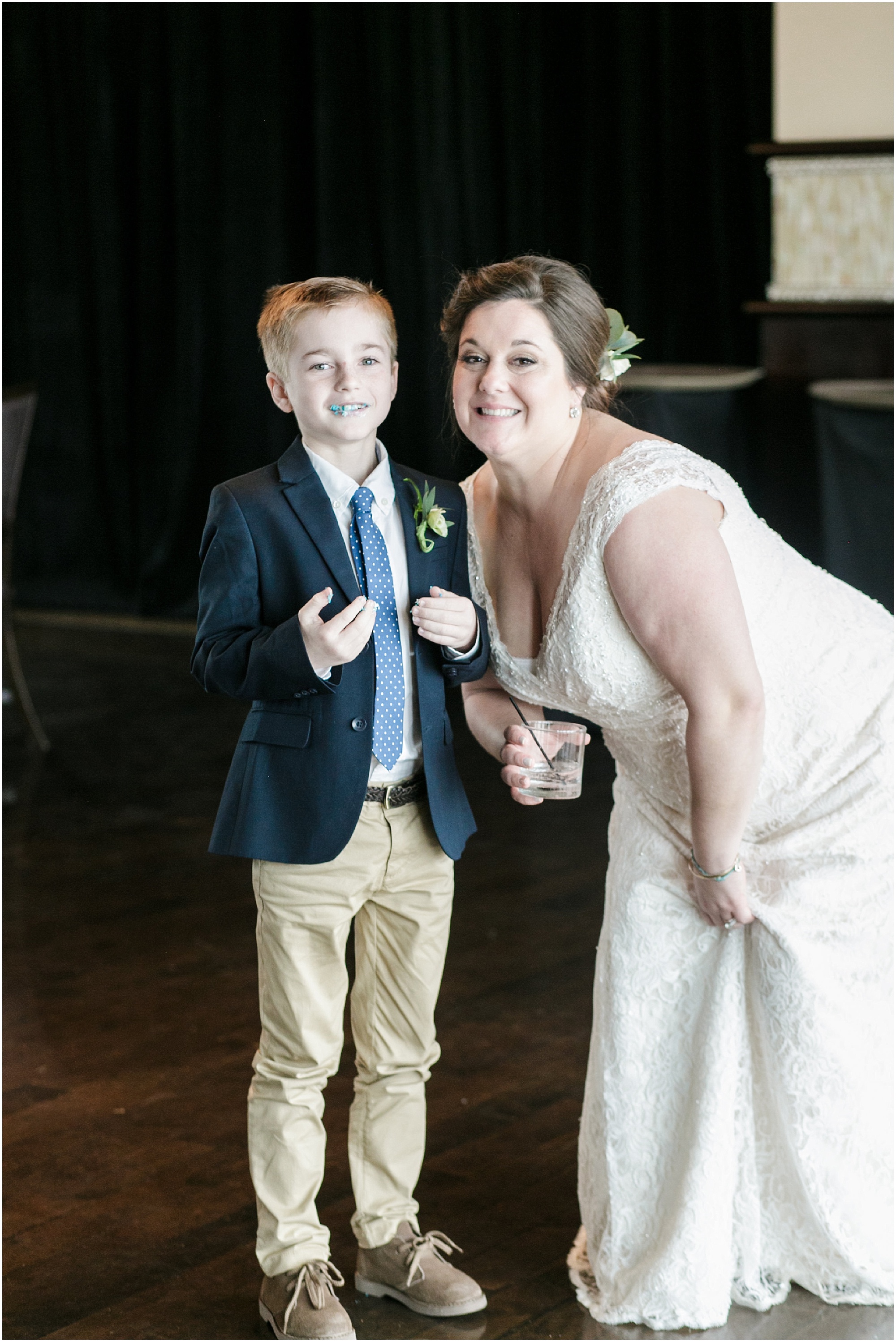 Bride poses with her son who has cake on his face. 