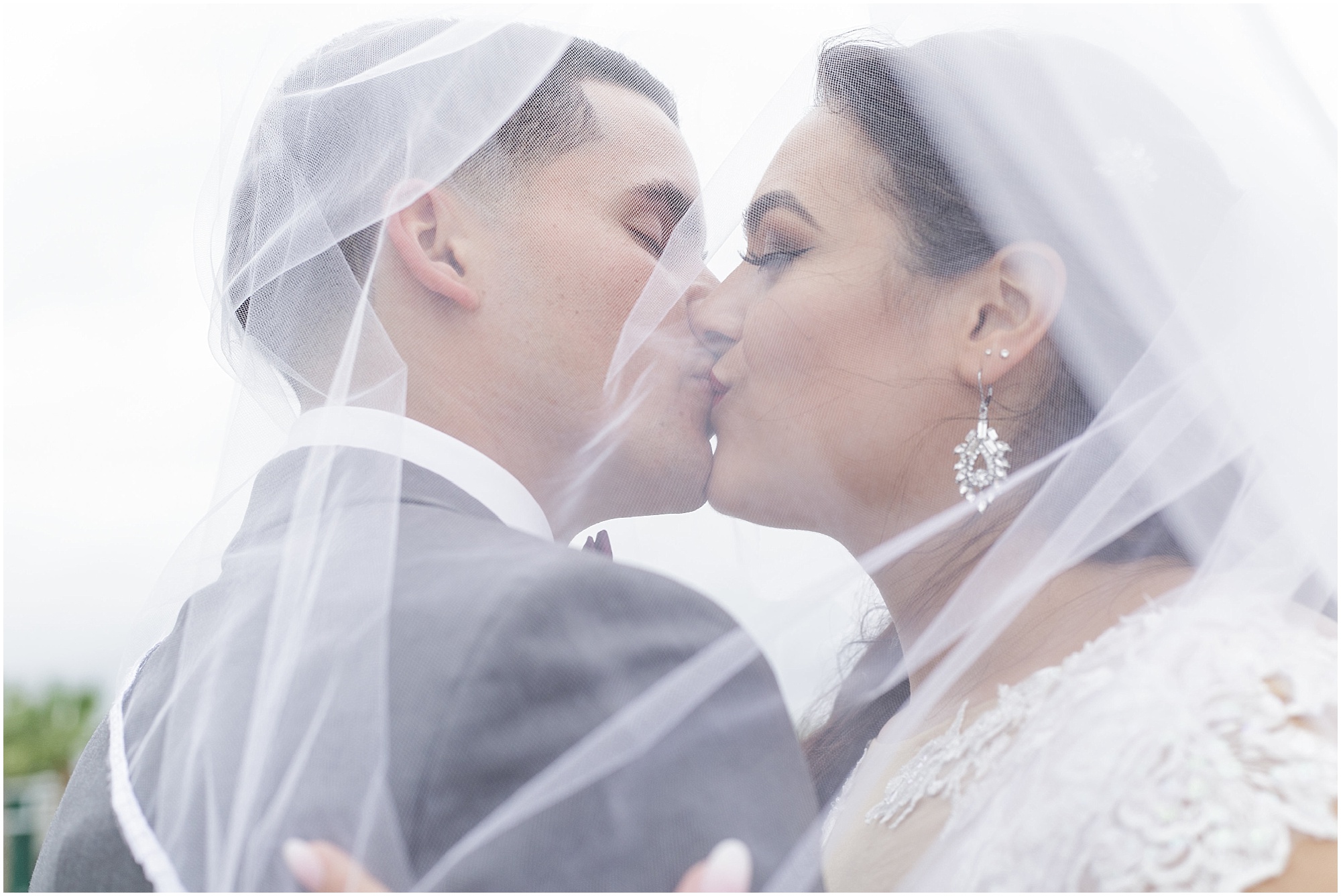 Bride and groom kissing while covered in her wedding veil. 