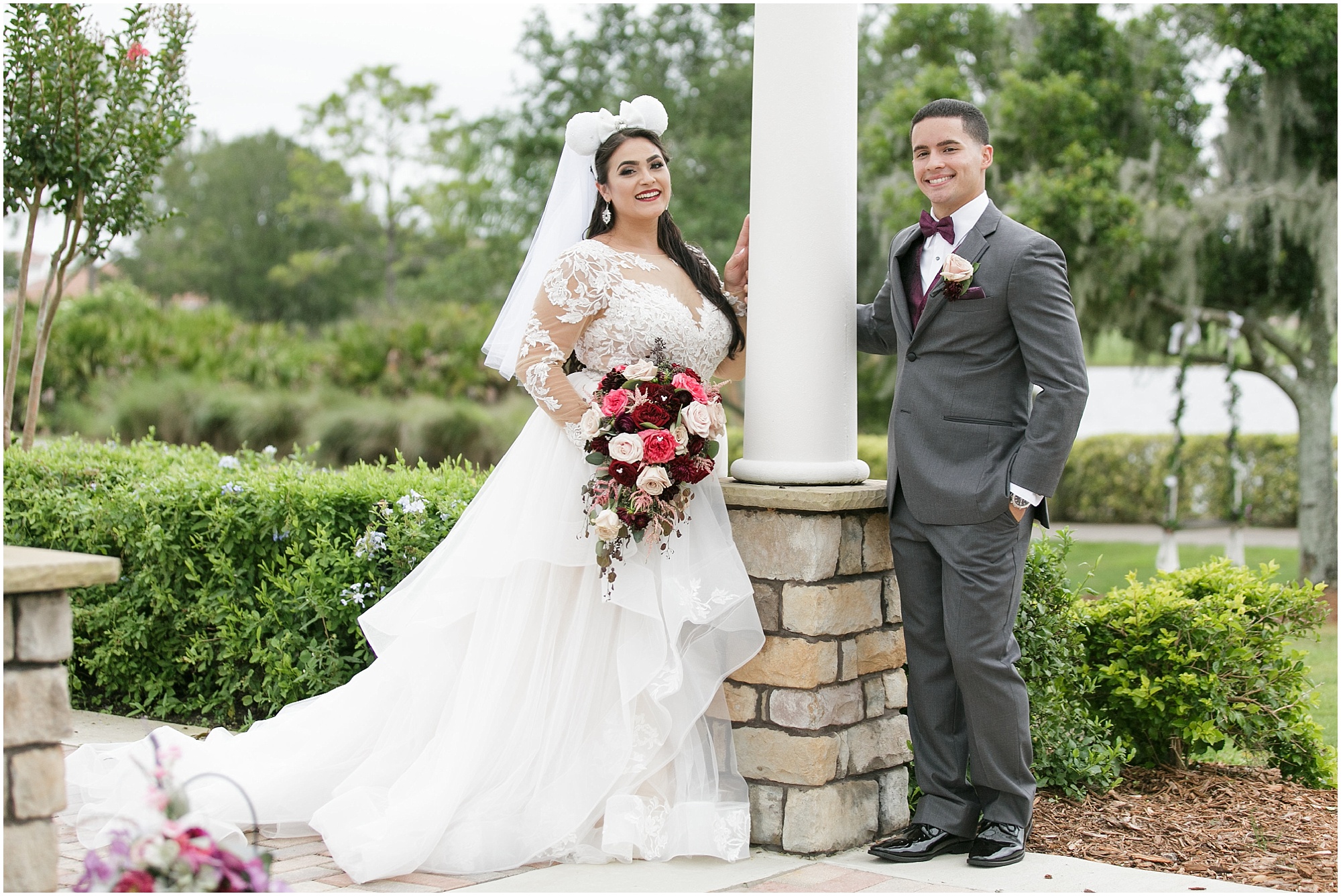 Bride wearing her Mickey ears takes photos with her groom outdoors. 