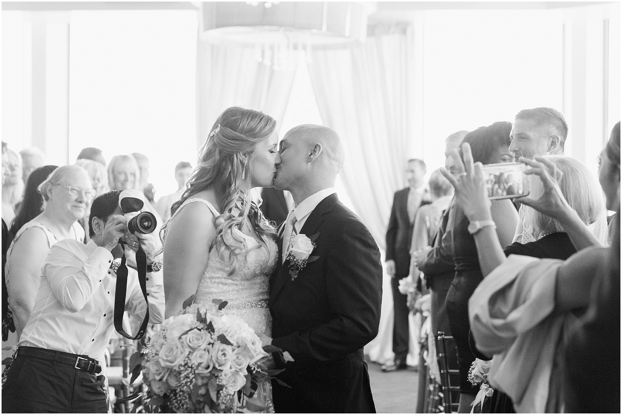 Black and white photo of the bride and groom kissing when they walking down the aisle. 