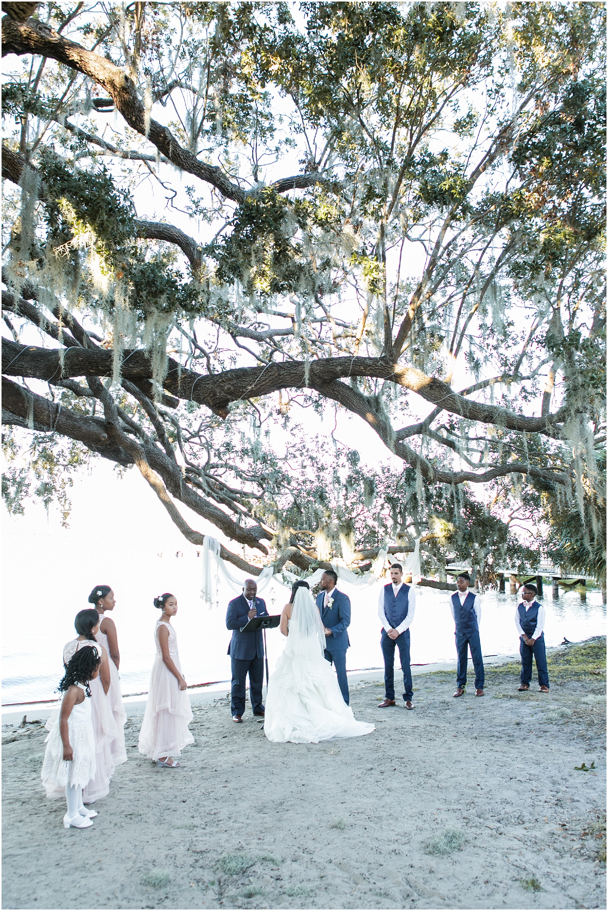 Photo of a wedding taking place under a large oak tree on the lakeshore. 