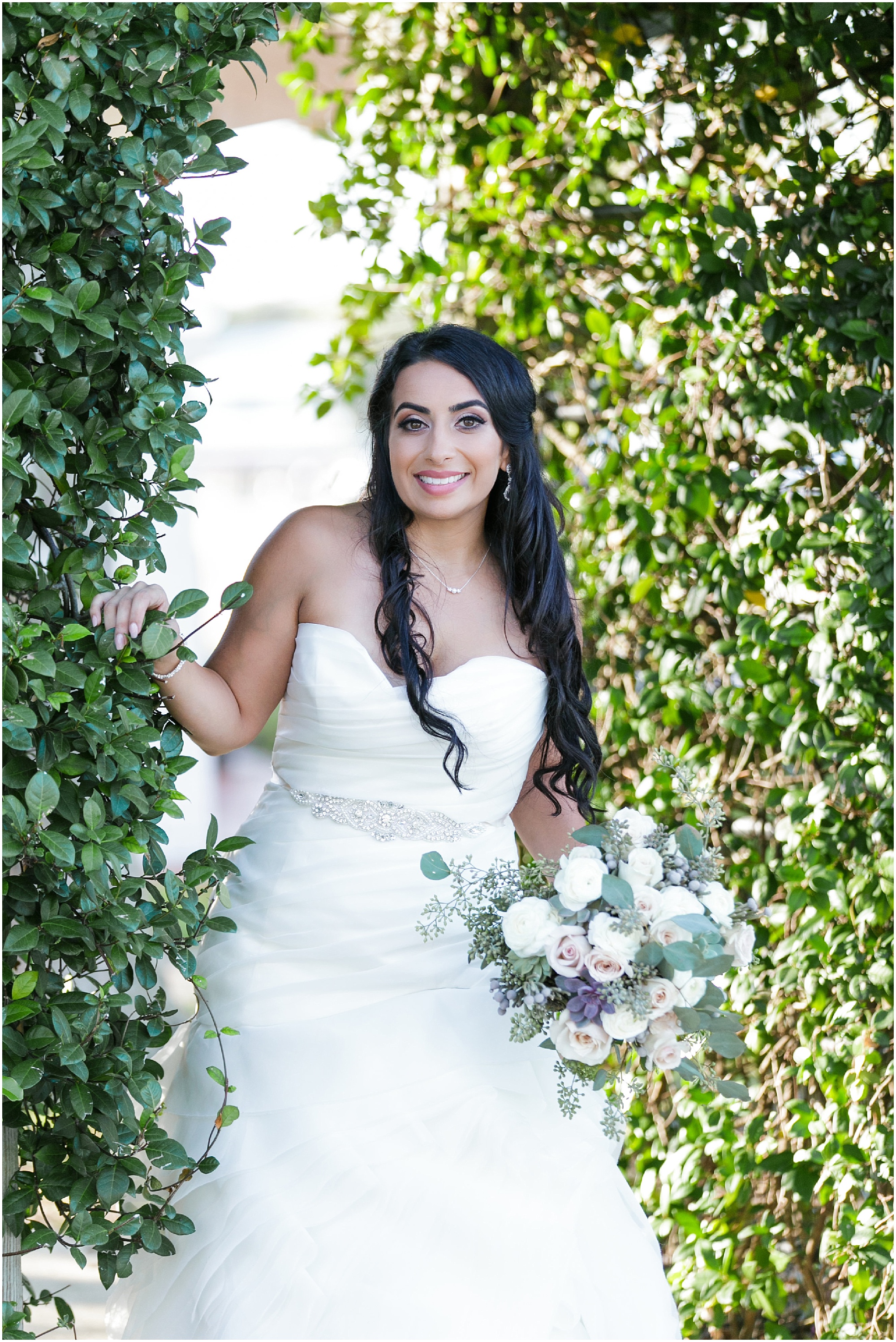 Bride standing under an archway of greenery in her wedding dress. 