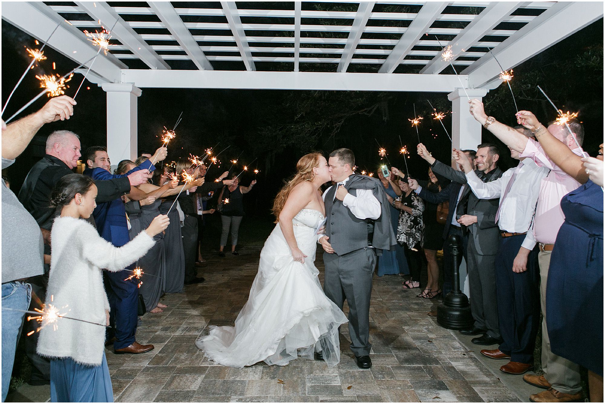 Bride and groom kiss while guests make a tunnel of sparklers. 