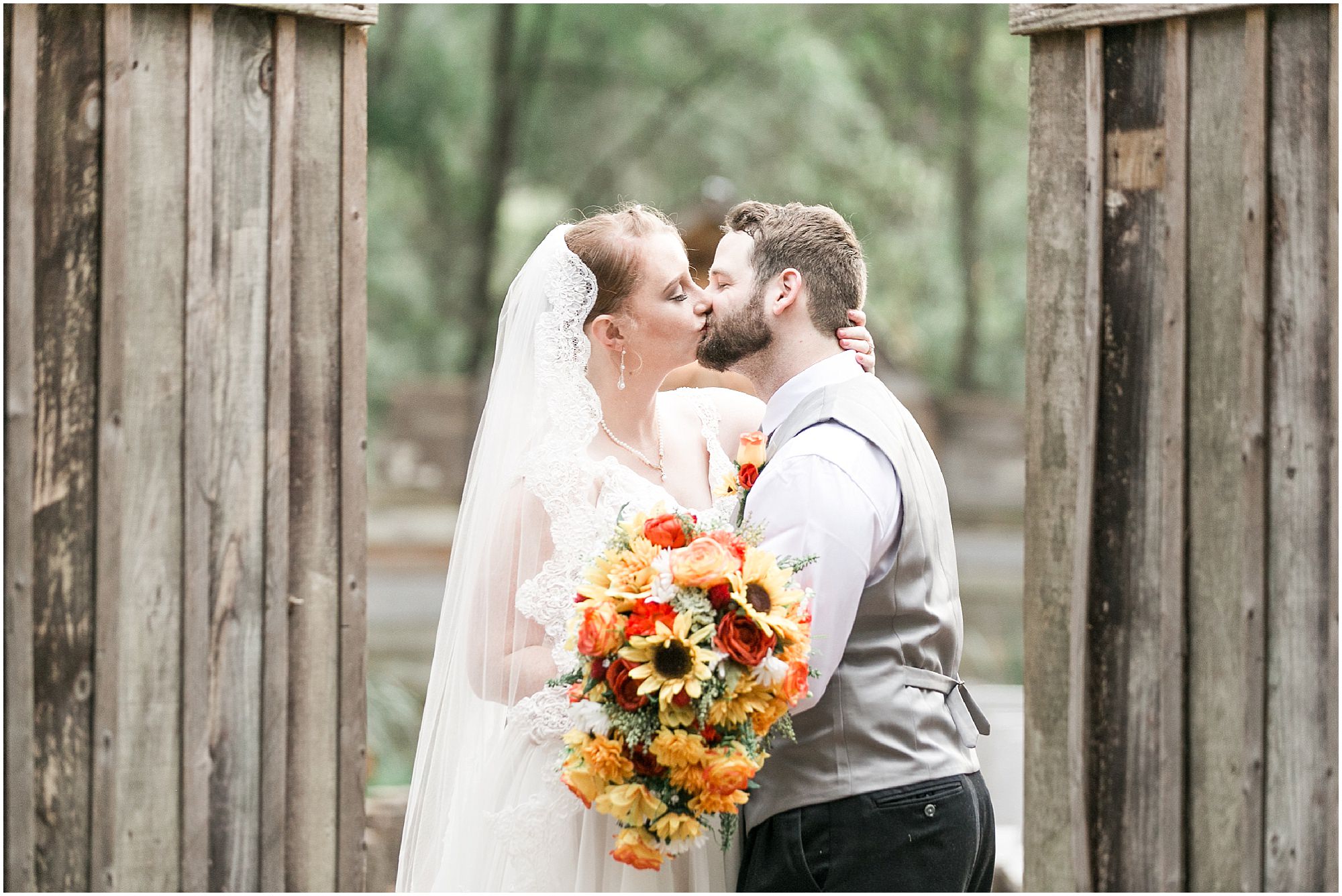 Bride and groom kissing by a wooden fence.