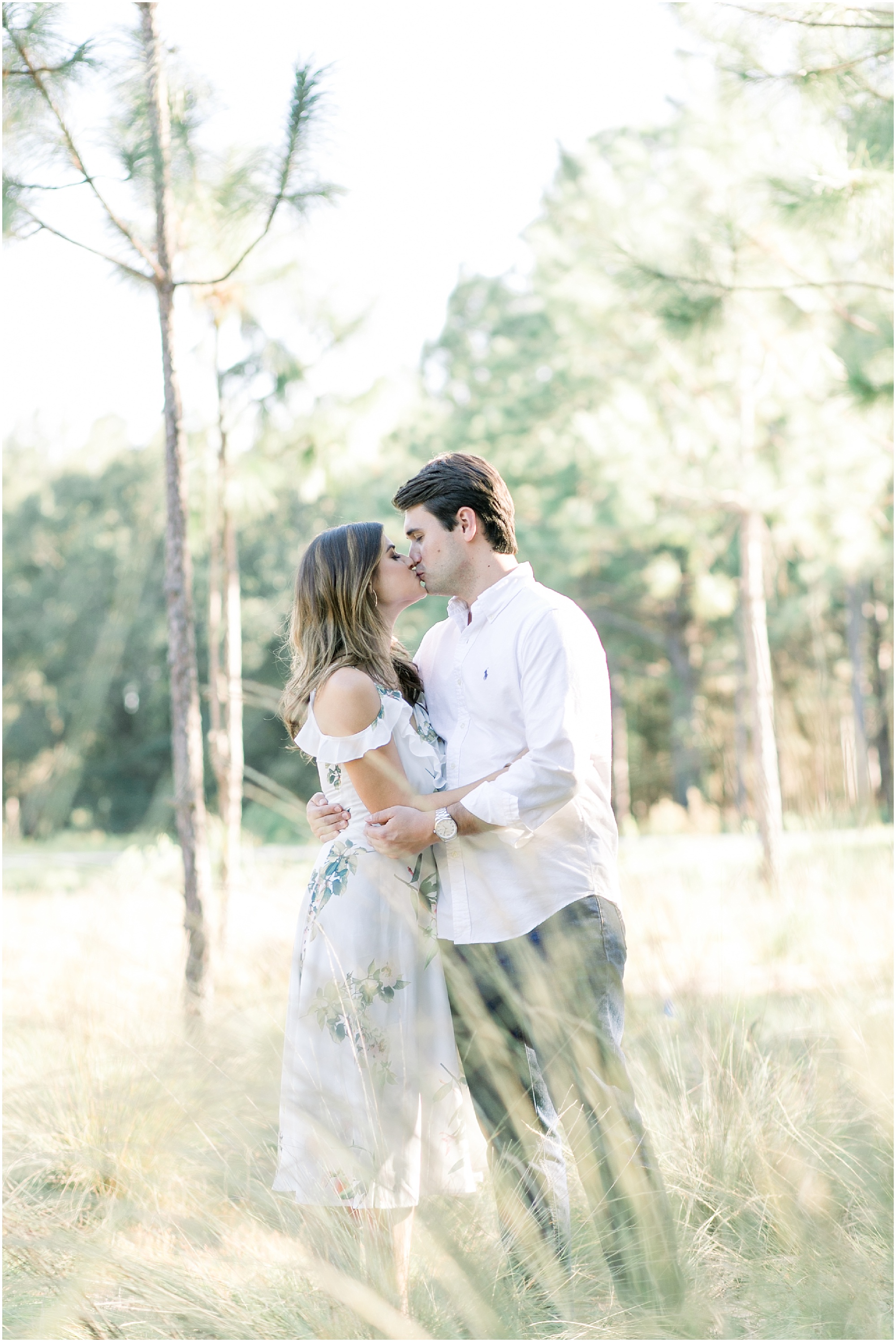 Couple kissing while standing in between trees at their sunny autumn engagement session