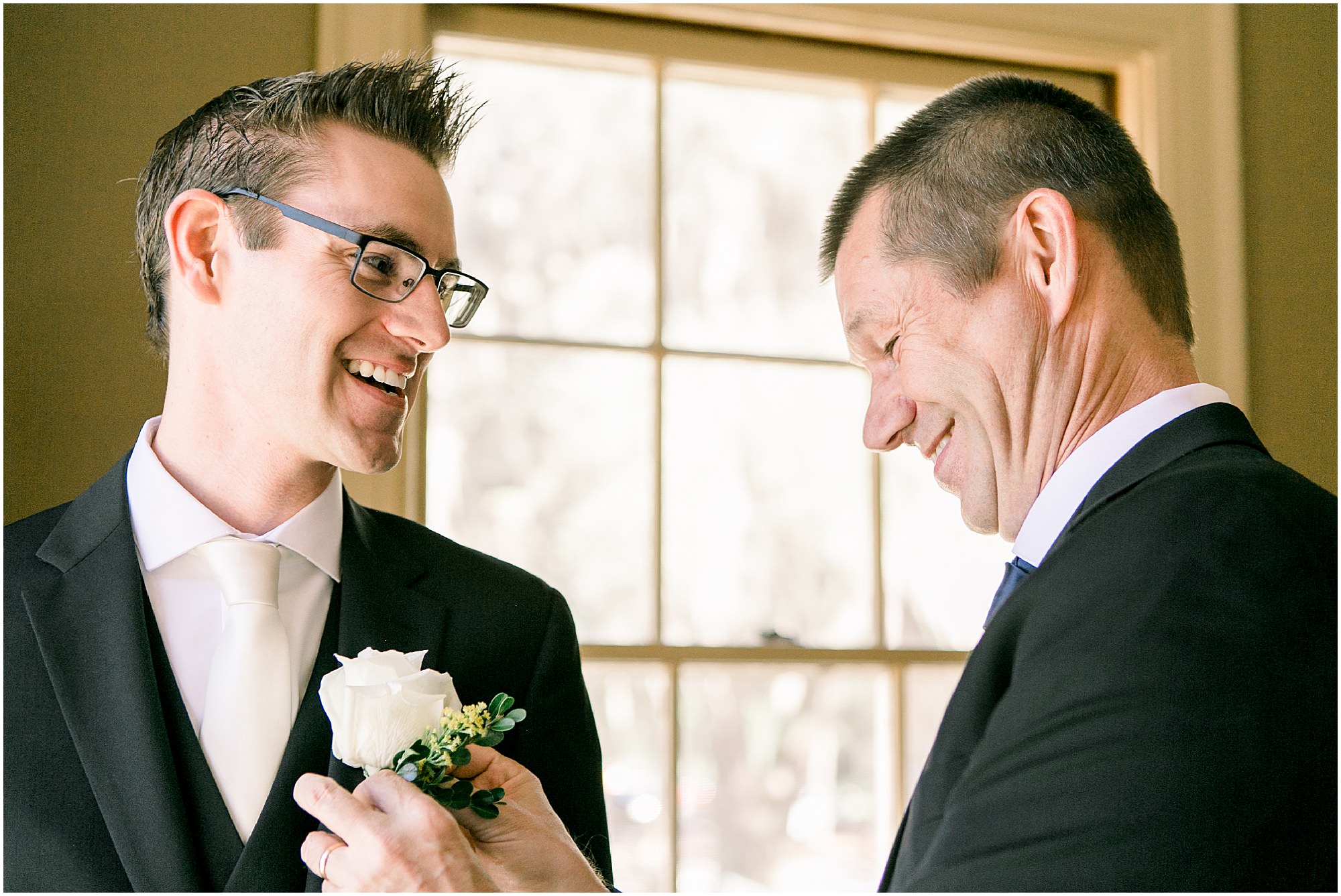 Groom's father helping him put on his boutonniere. 