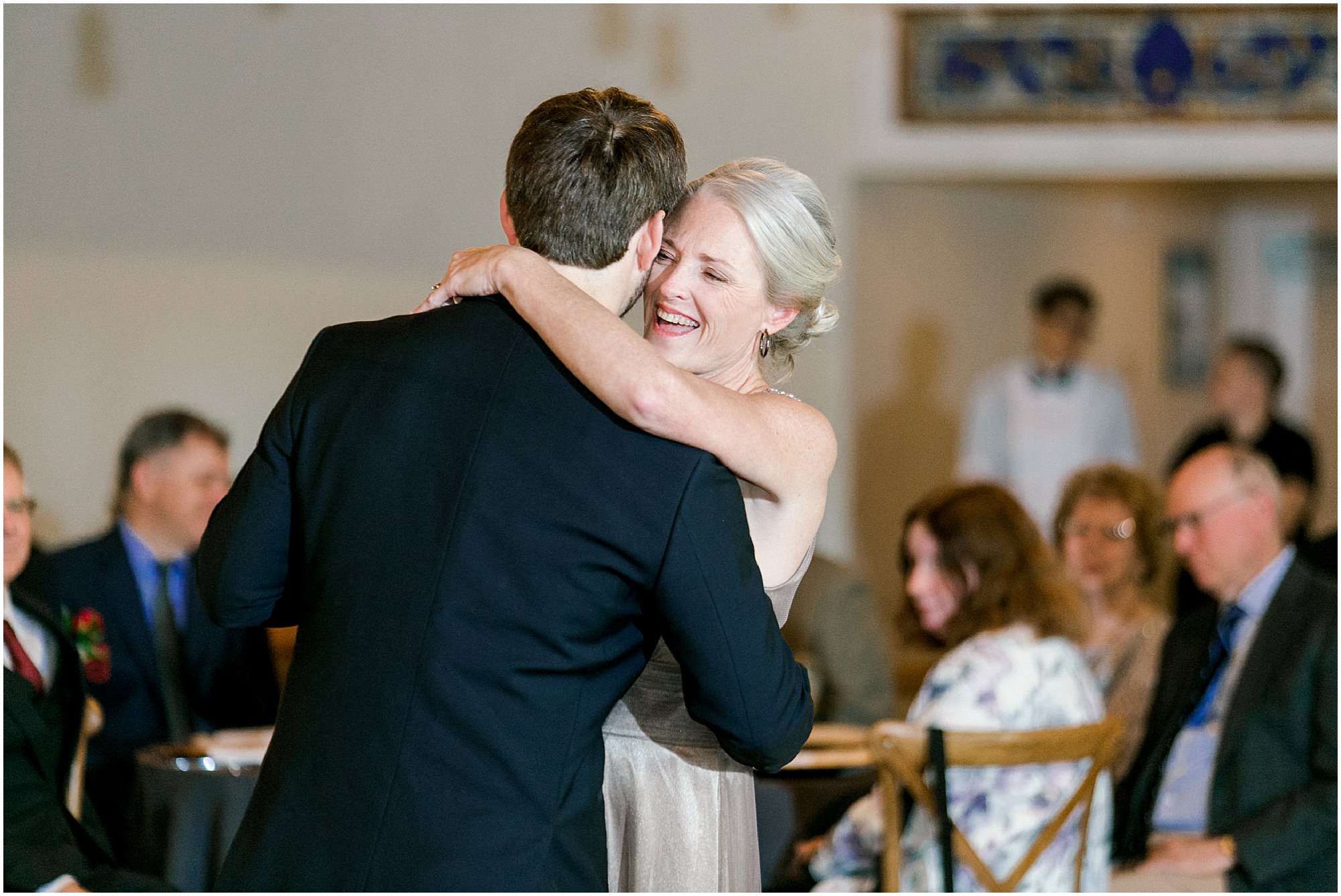 Groom's mother laughing as she dances with him. 