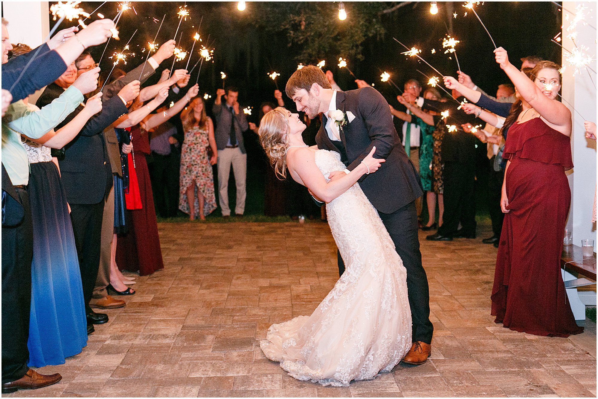 Groom dips the bride as guests wave sparklers as they leave wedding. 