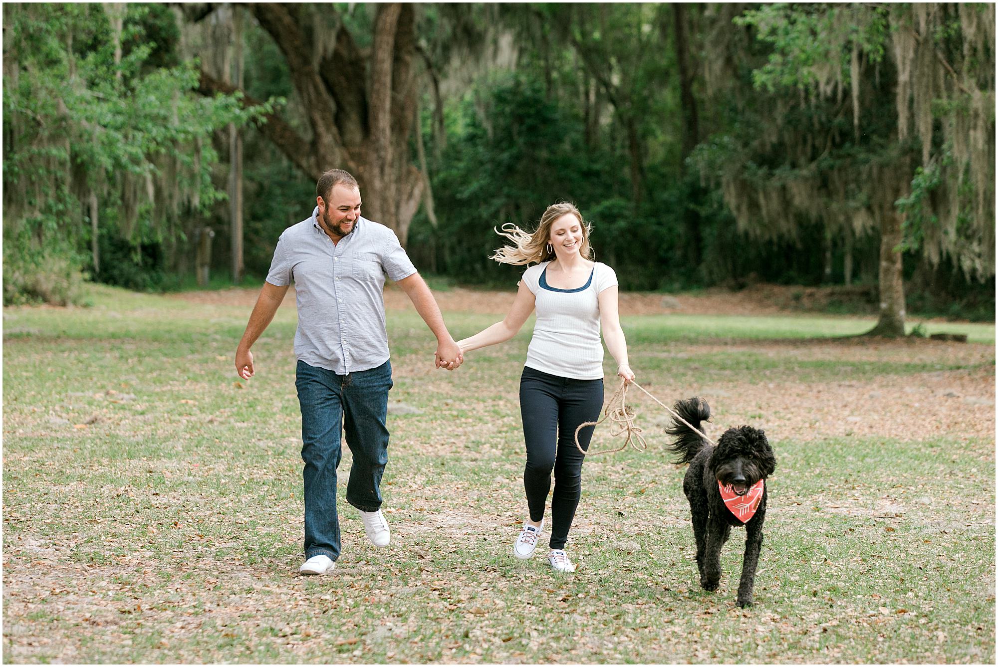 Couple running through the park with their dog at engagement session