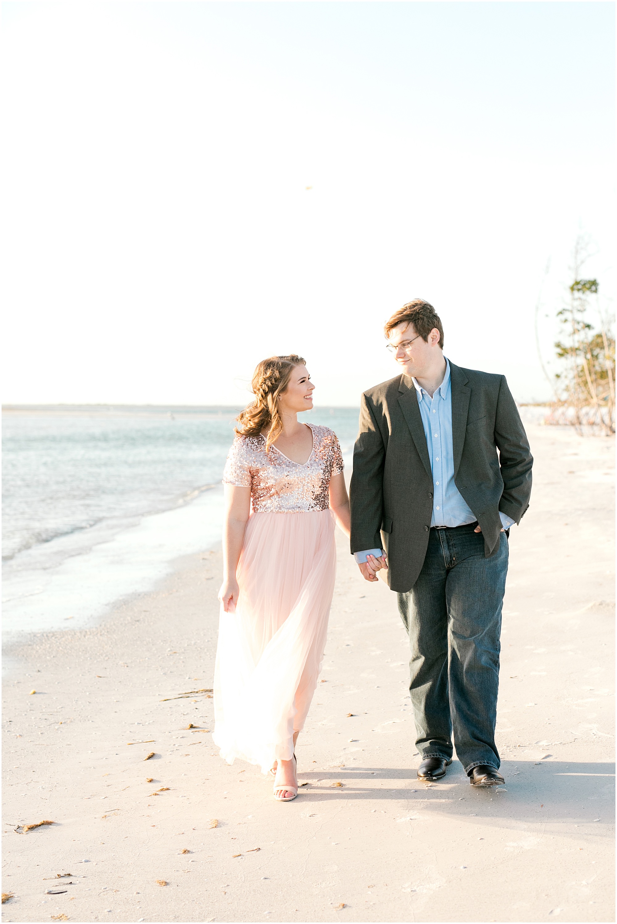 Couple hold hands and walk down the beach at Sweet Fort De Soto Engagement Session