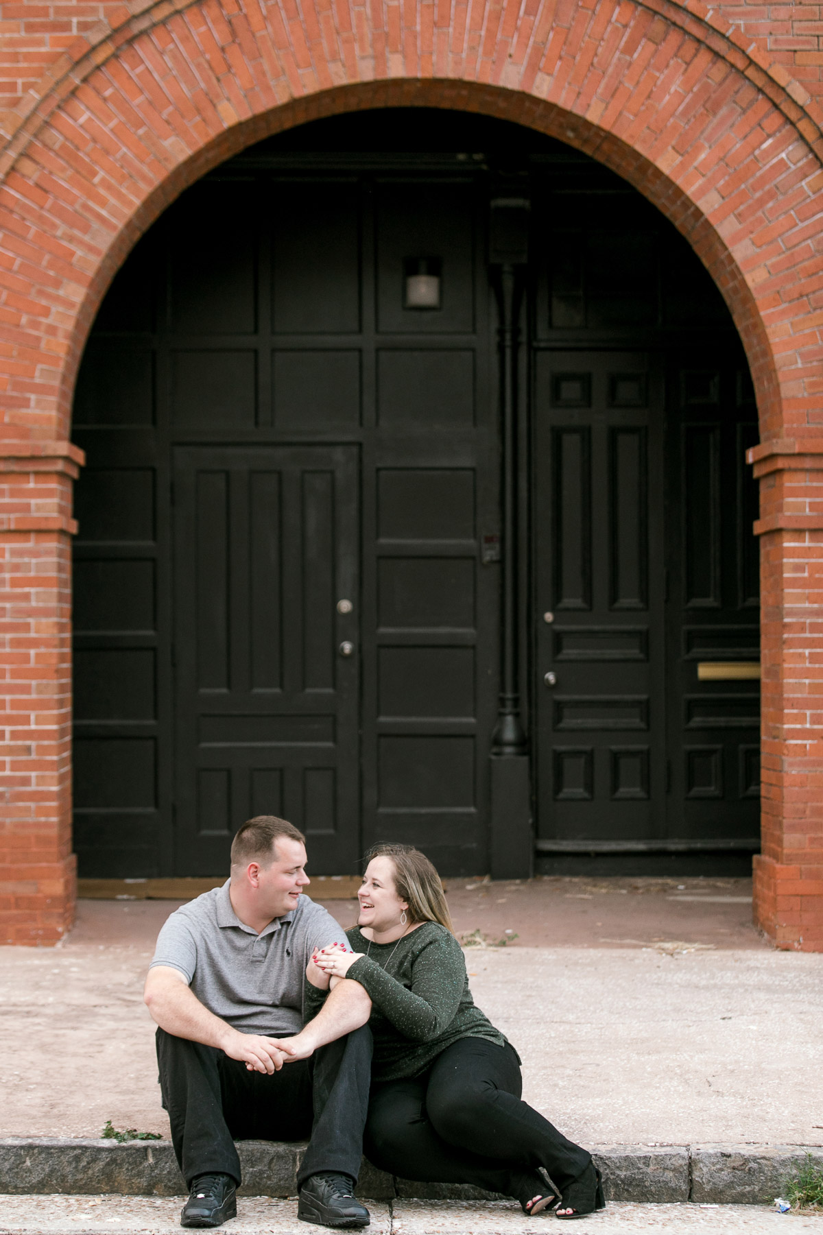 Couple sitting and laughing on a curb in front of historic brick building