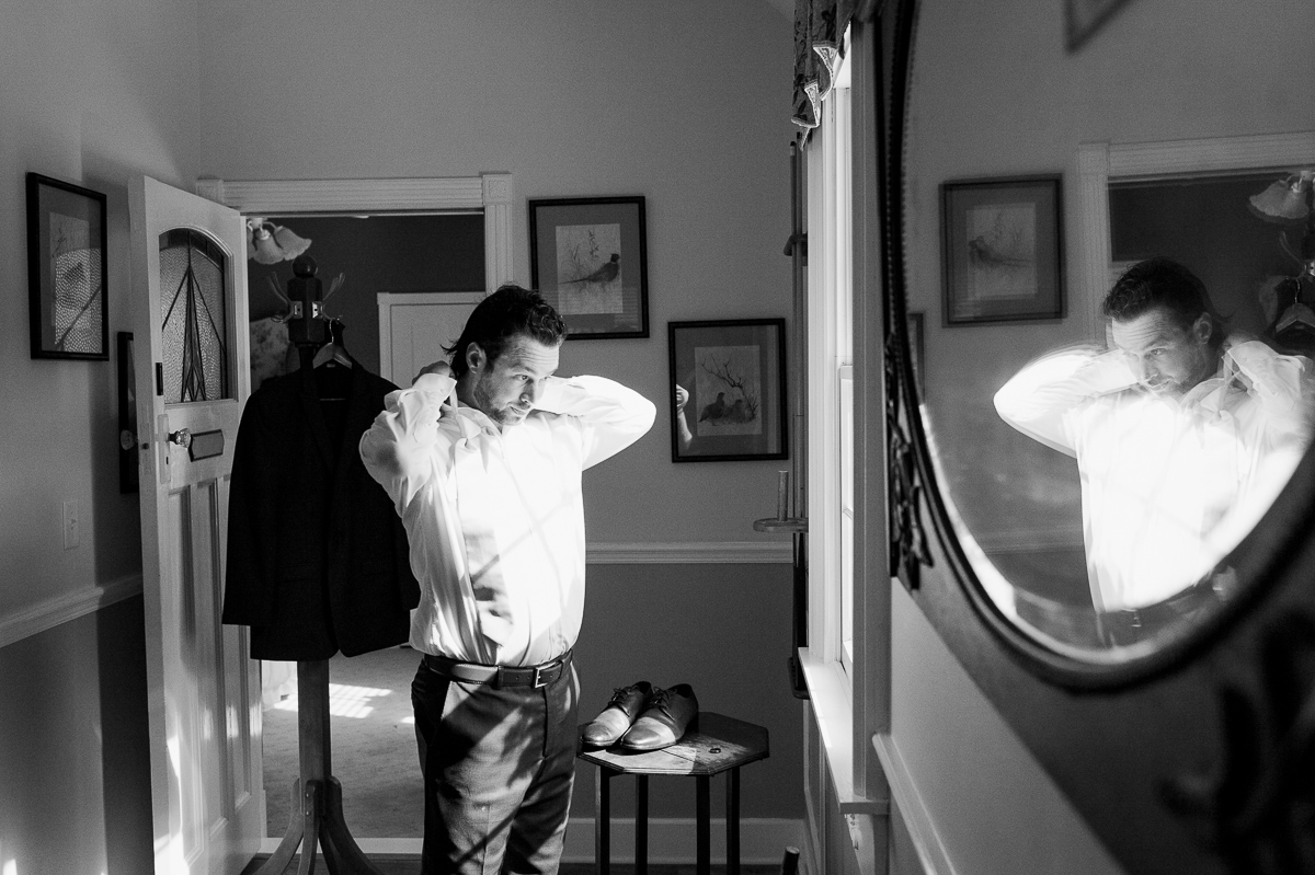 black and white photo of groom fixing his collar 