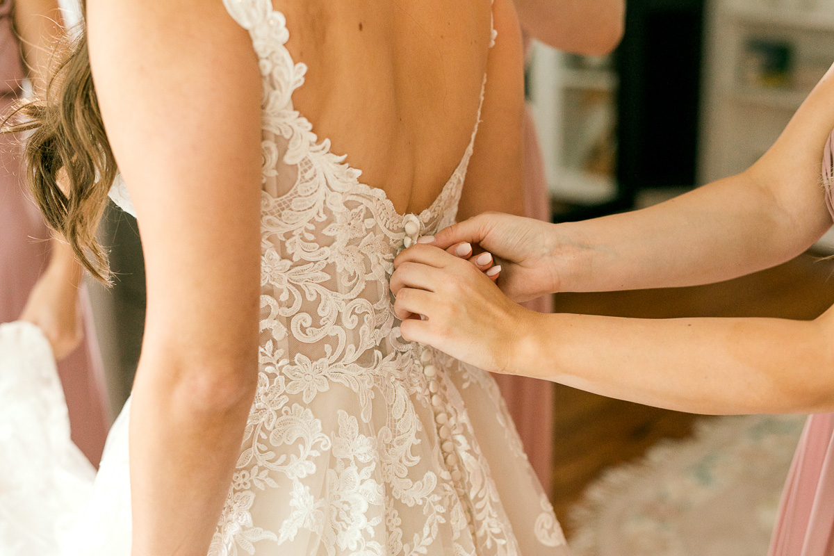 bride having her wedding dress buttoned up by bridesmaid