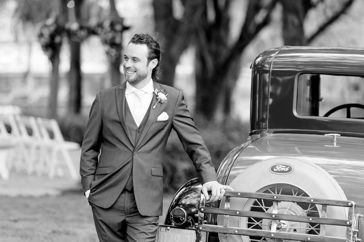 Black and white photo of groom standing with an old Ford antique truck