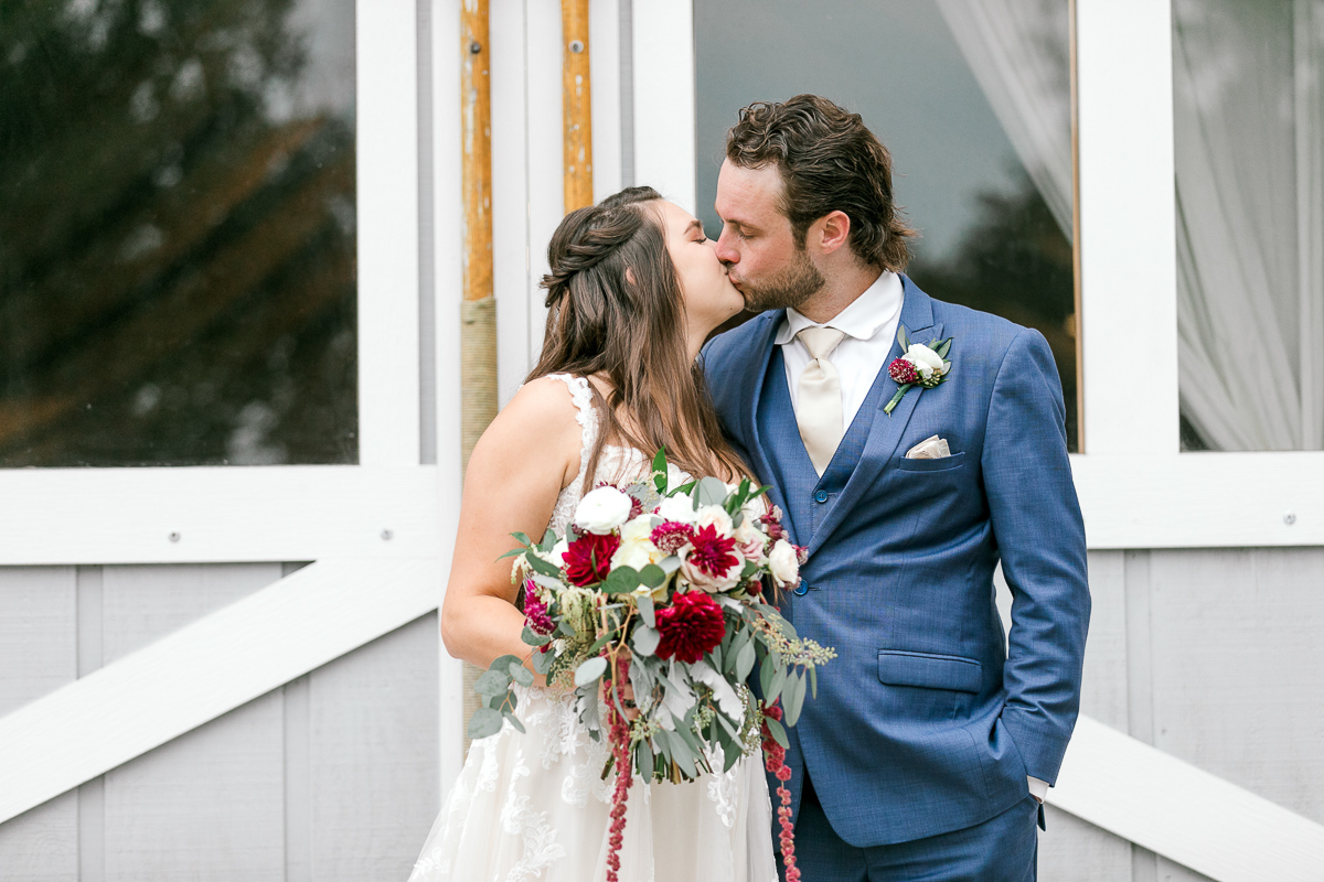 bride and groom kiss in front of boathouse doors