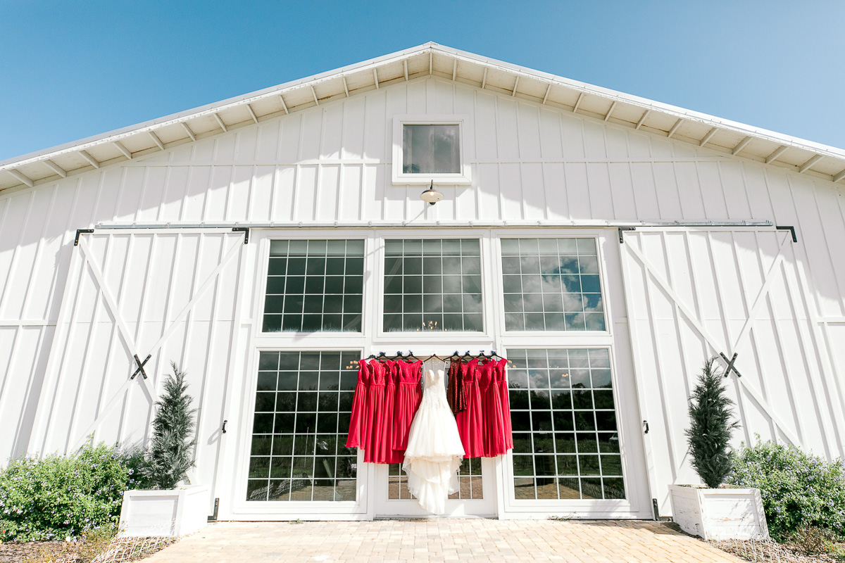 Romantic Ever After Farms Wedding, brides dress and red bridesmaids dresses hanging from large windows. 