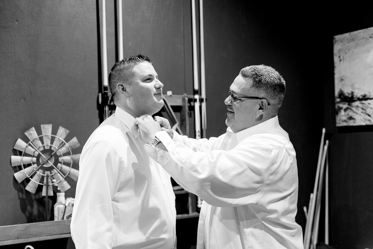 Black and white photo of the father of the bride helping the groom get ready 