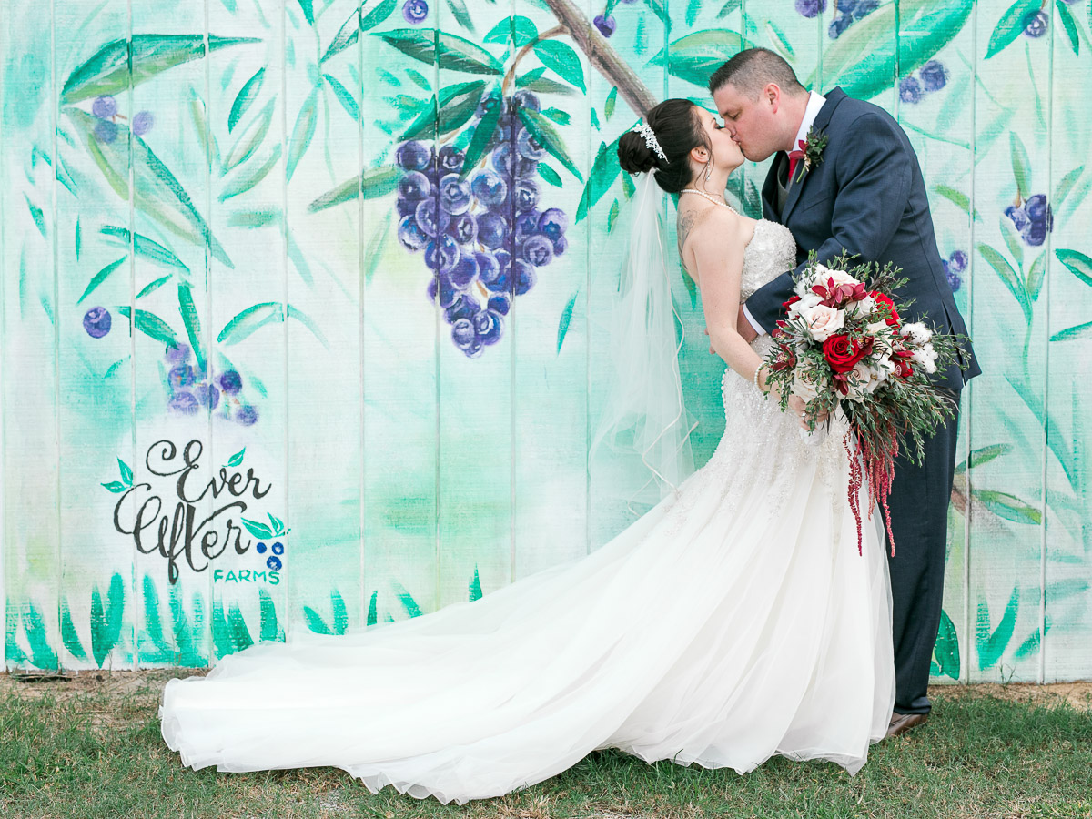 Bride and groom kiss in front of custom painted fence at 